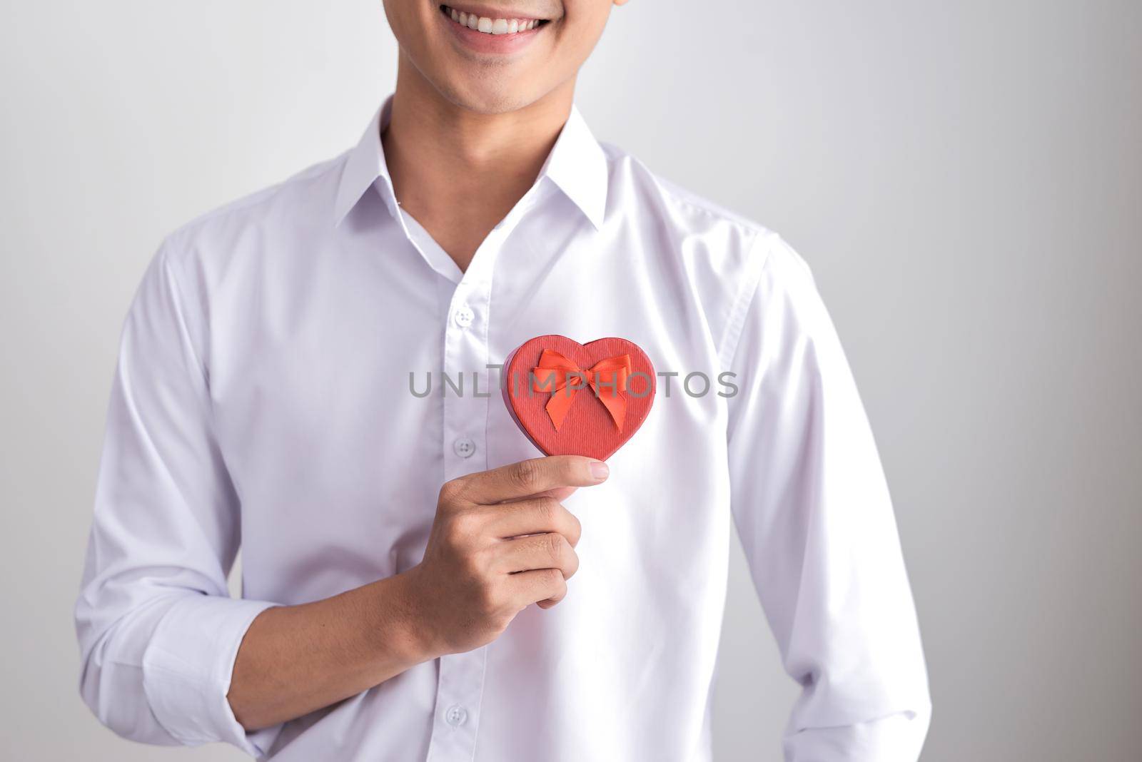 A gift for the beloved. Young beautiful smiling elegant man in a white shirt holding a box with a gift and shows it to the camera. Valentine's Day. by makidotvn