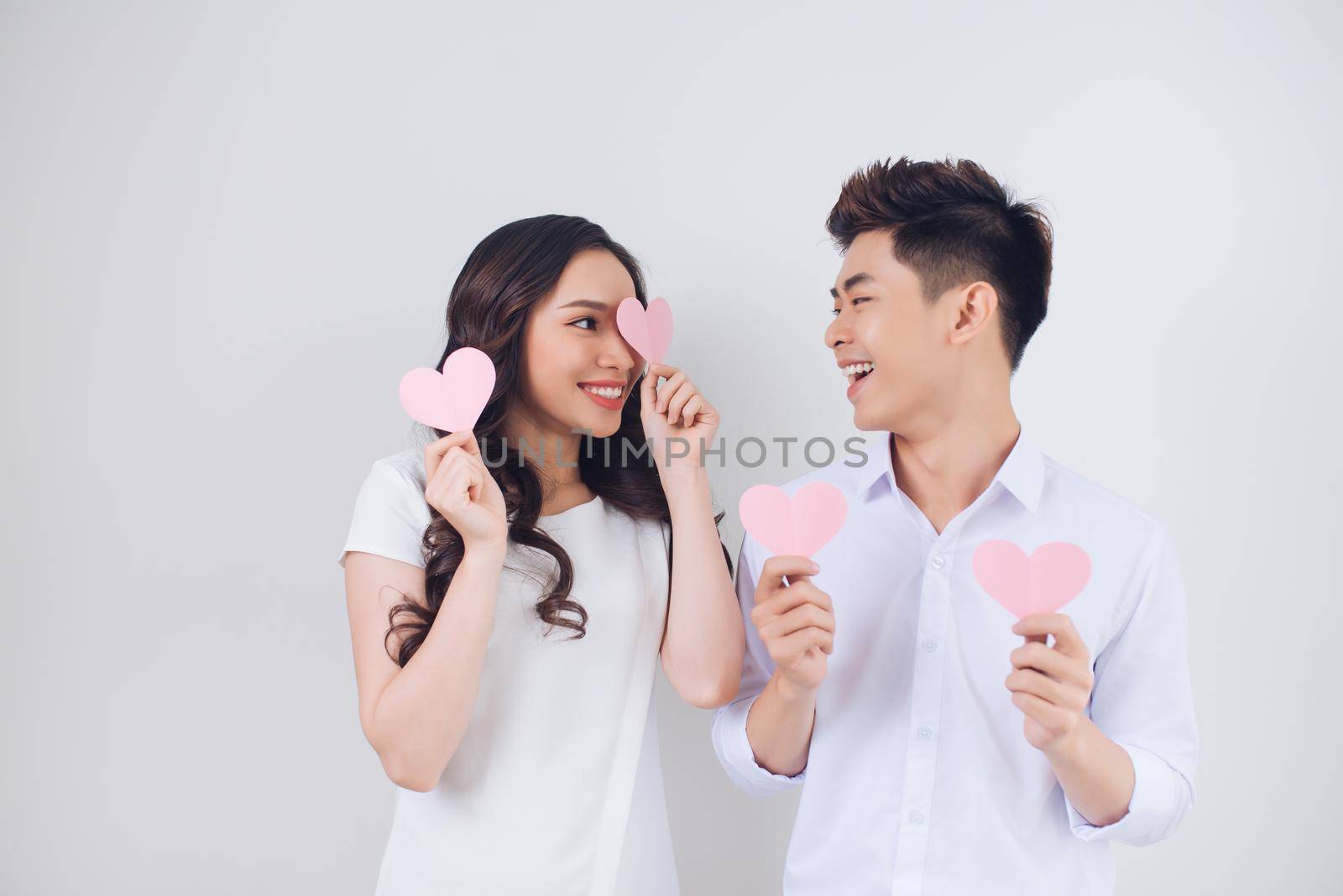 Happy young Vietnamese couple is holding pink paper hearts and smiling by makidotvn