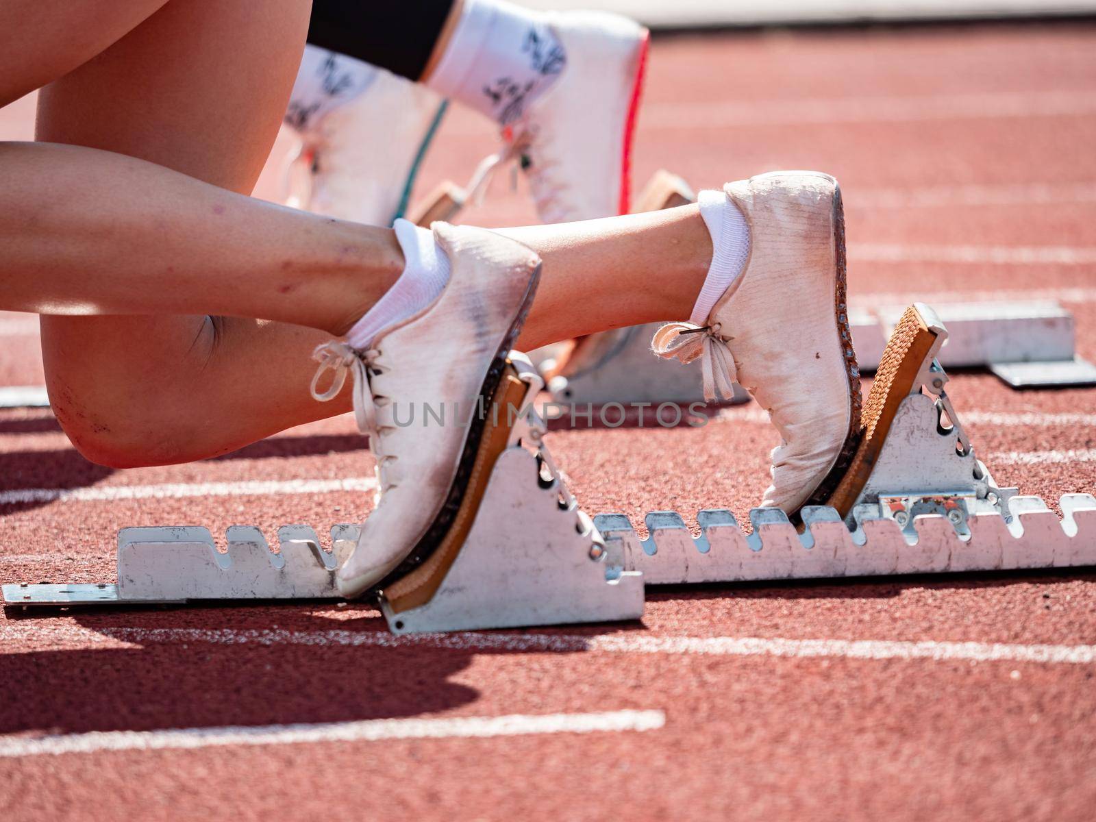 Side  view of female feet on starting block ready for a sprint start. Naked female legs in light running shoes.