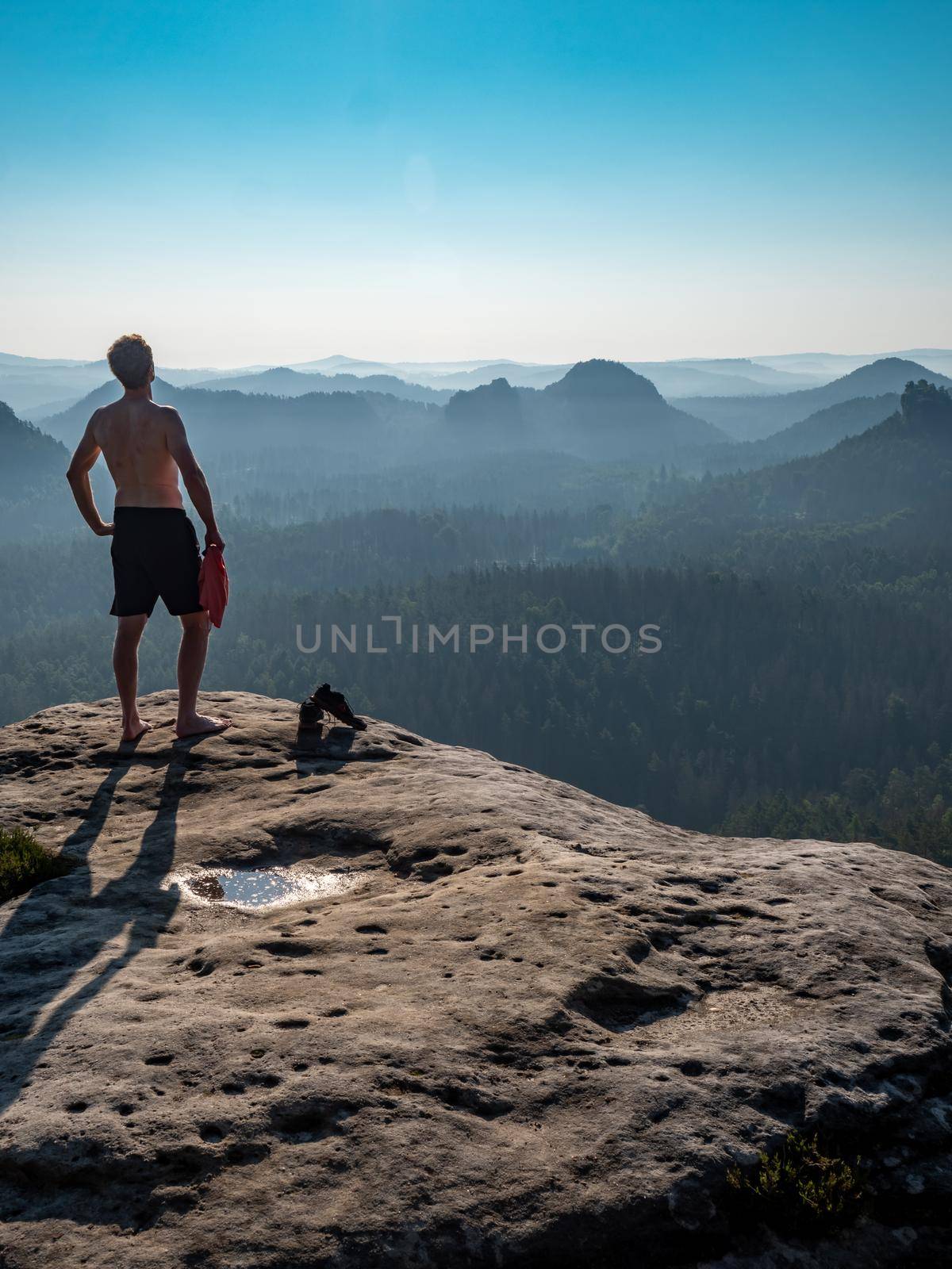 Shirtless man with a sporty figure on the edge of a rock enjoys the view by rdonar2
