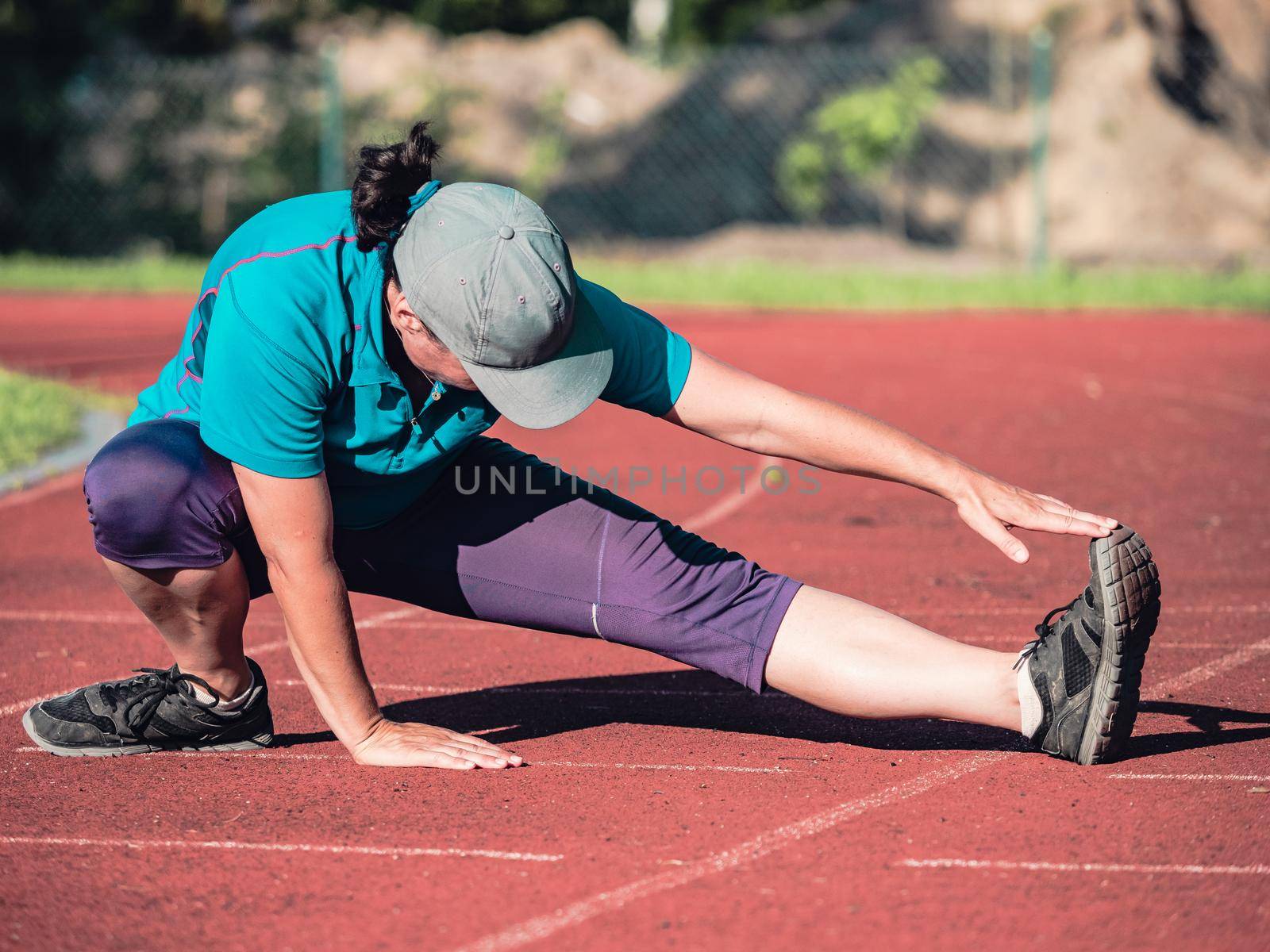 Athletic middle aged woman stretching on red  running track before training, healthy fitness lifestyle 