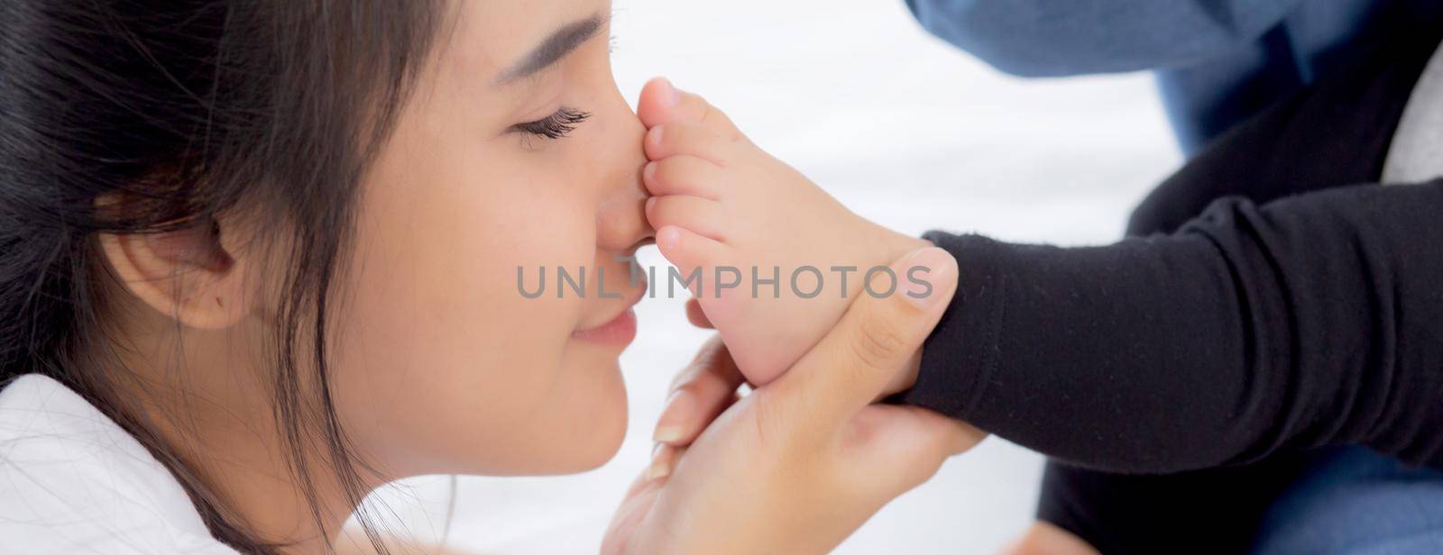 Young asian mother kiss foot of little baby girl on bed in bedroom at home, mom and newborn with relationship and bonding together, motherhood with love and care child with happy, family concept.