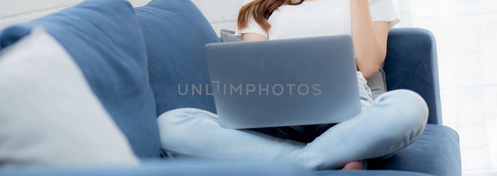 Young asian business woman smile and work from home with laptop computer online on sofa in living room, freelance girl using notebook on couch, new normal, lifestyle concept. by nnudoo