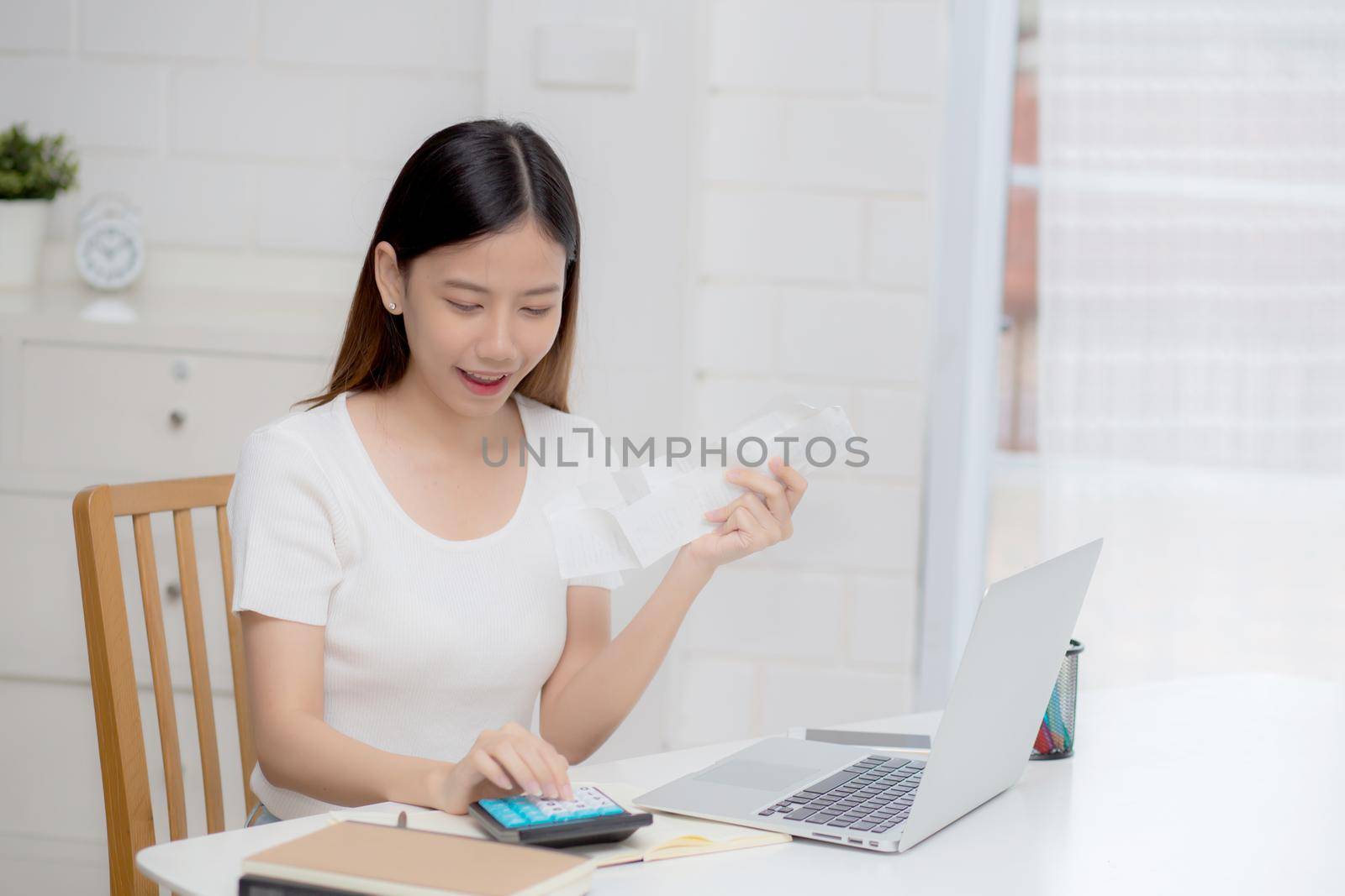 Young asian woman calculating finance household with calculator on desk at home, girl checking bill and success for saving expenses household, debt closure, tax and accounting, business concept.
