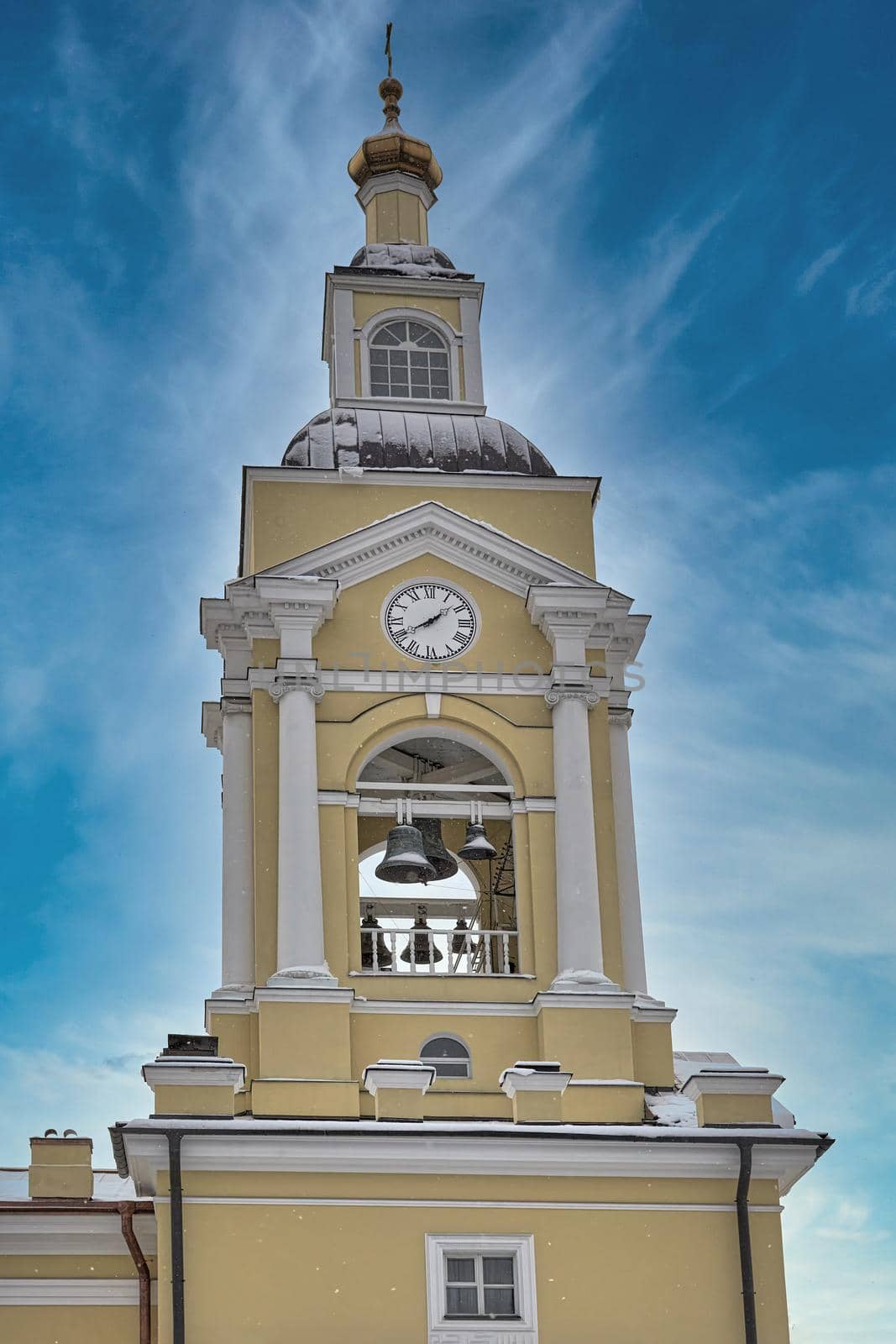 Christian church with a bell tower and a clock tower against a blue sky. Religious yellow building with a tower