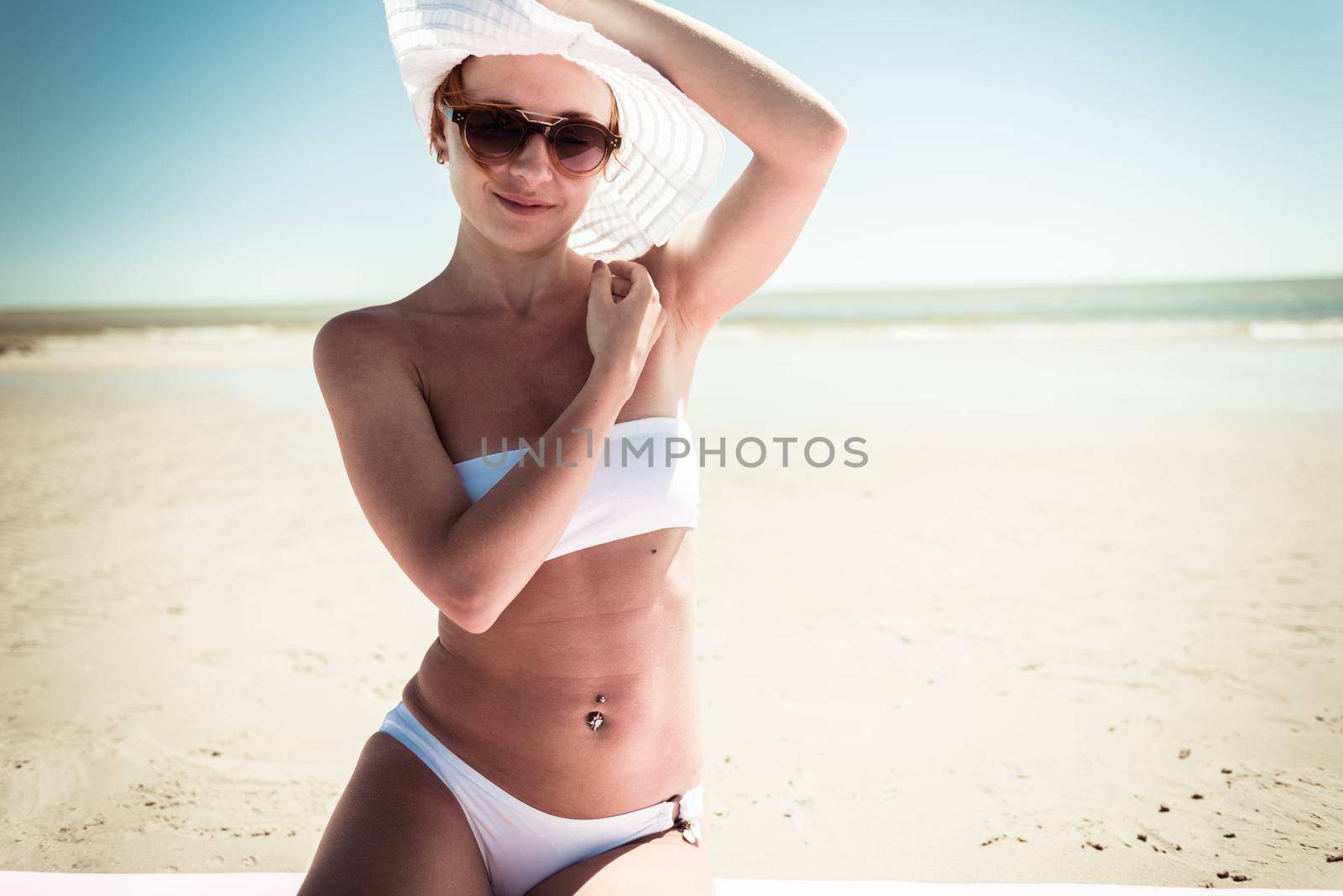 Beautiful red woman wearing bikini standing on the beach enjoying the sun