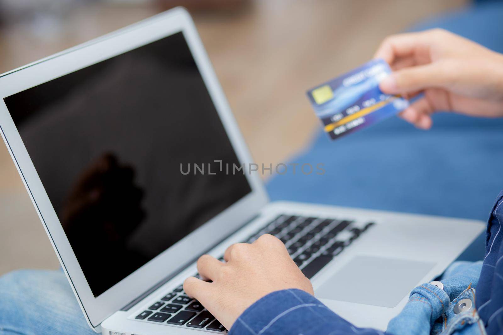 Hand of young man using laptop computer display blank screen shopping online with credit card on sofa at home, male purchase and payment with debit card, e-commerce and technology, lifestyle concept. by nnudoo