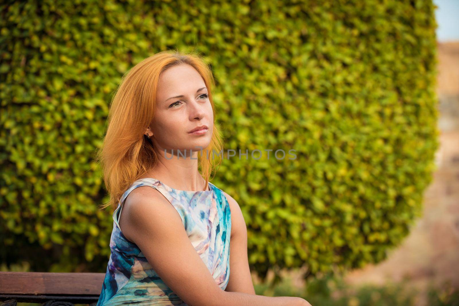 Young red woman wearing long dress sitting on a bench