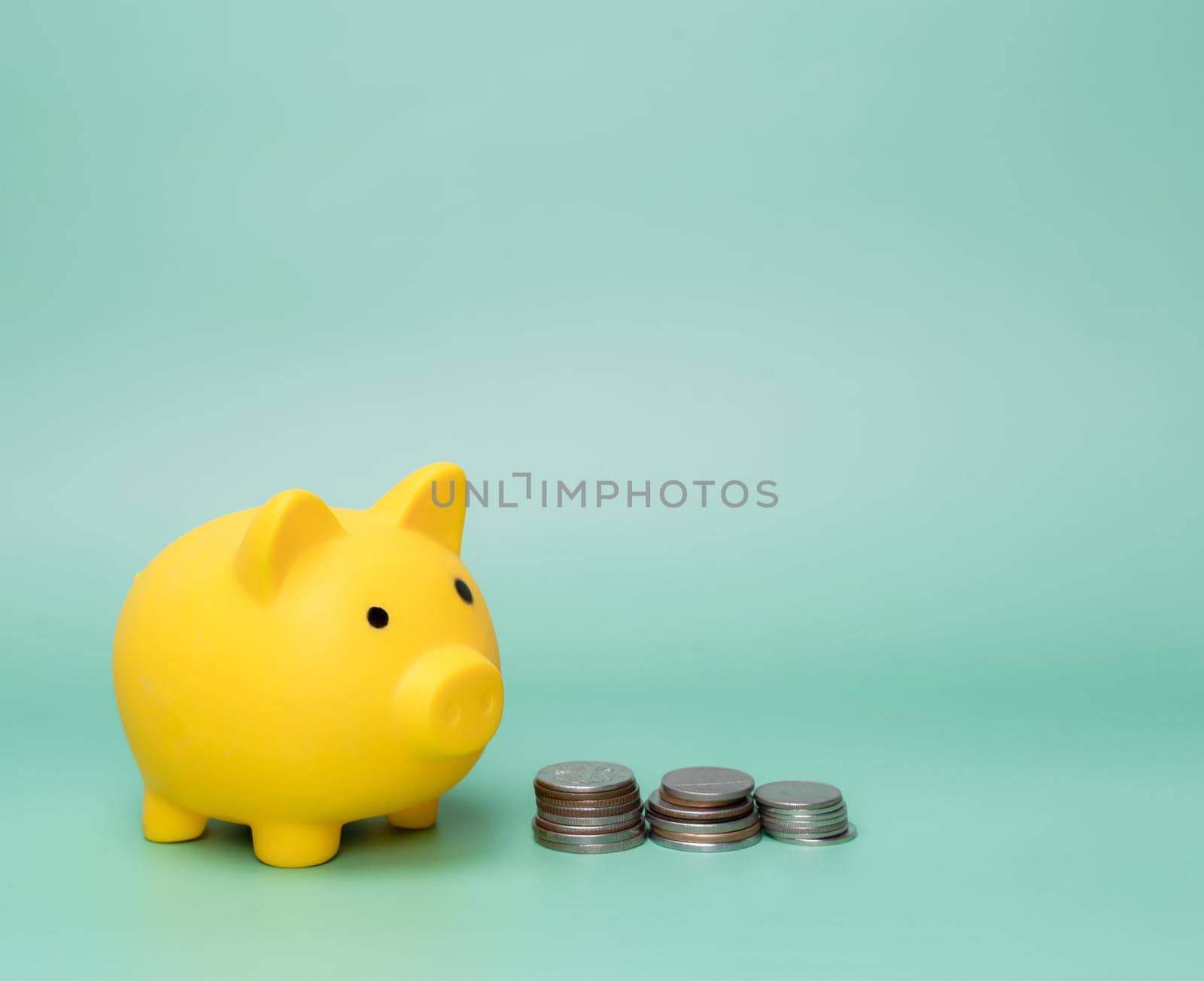 Yellow piggy bank and stack coins on green background