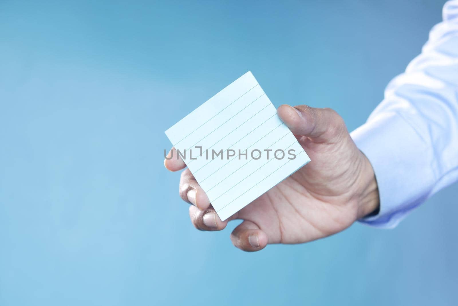 man hand hold a sticky note against blue background .