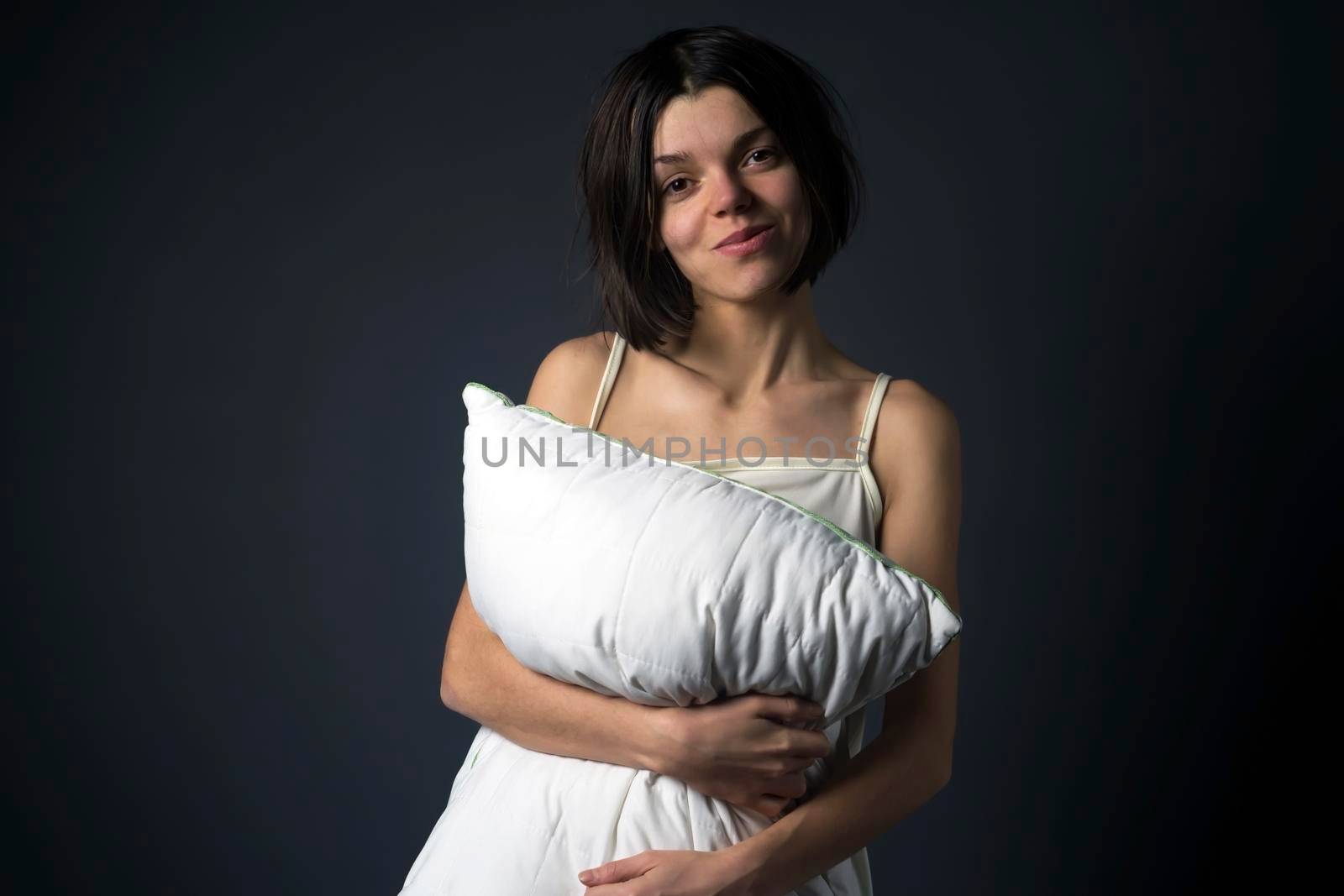 Sleepy funny young girl hugs a pillow, just woke up. The woman is tired after a working day and wants to sleep.