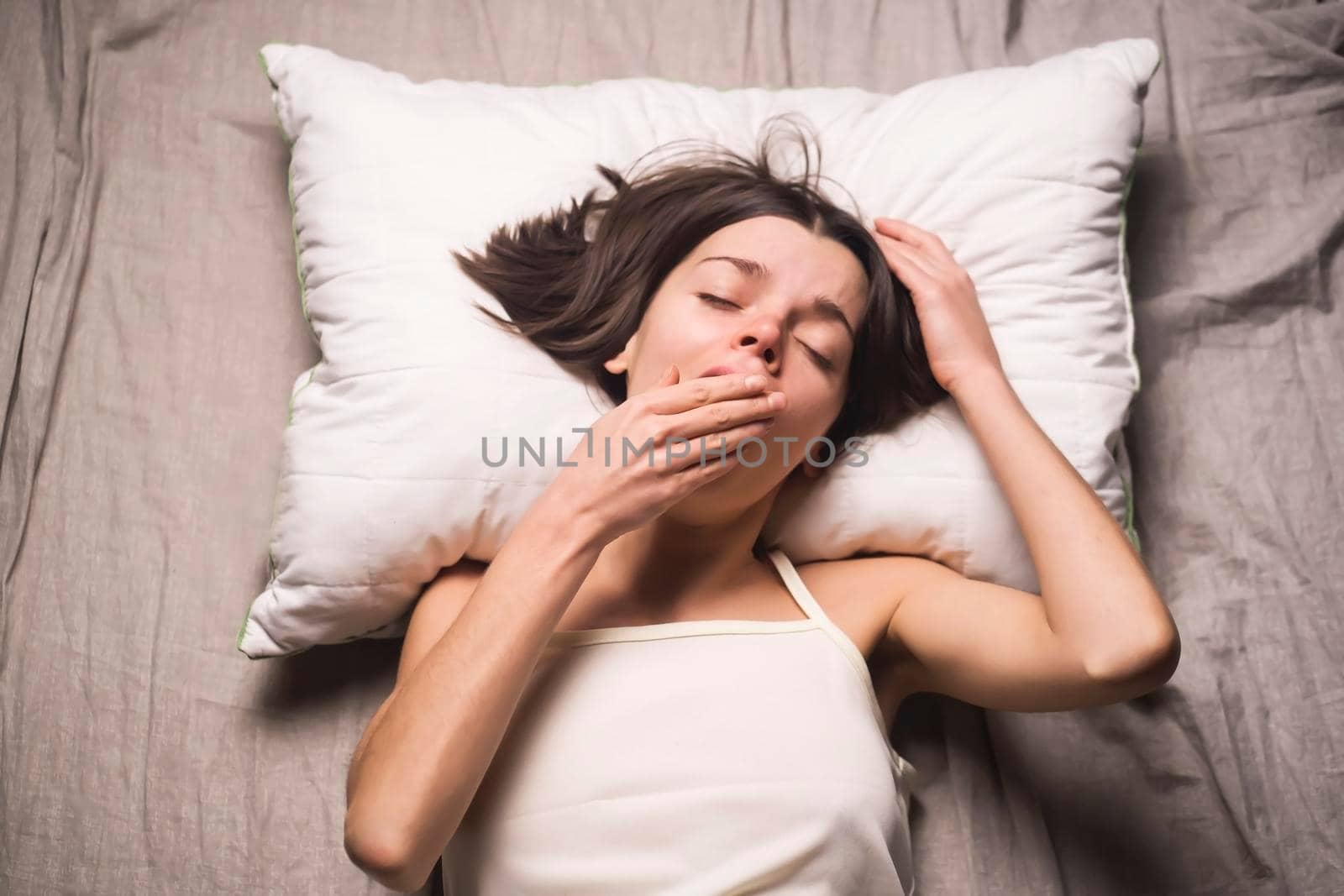 Young cute girl just woke up yawning in her cozy bed at home in the morning. Woman with her hair tousled on the pillow lazily procrastinates and does not want to go to work, prefers to sleep longer.