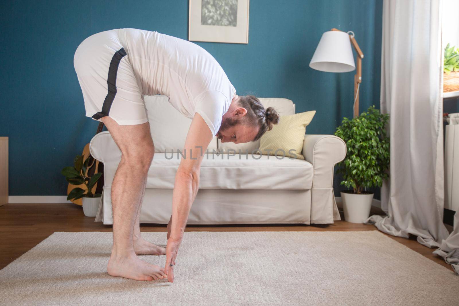 Mid adult mature man in white sport clothes practice yoga stretch doing exercise at home minimalistic scandinavian design room