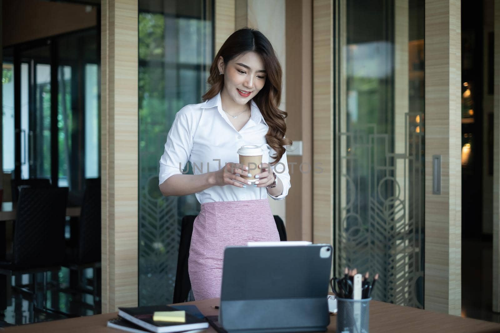 Portrait of cheerful asian woman wear white shirt looking at tablet on desk in office. Concept of young business people.
