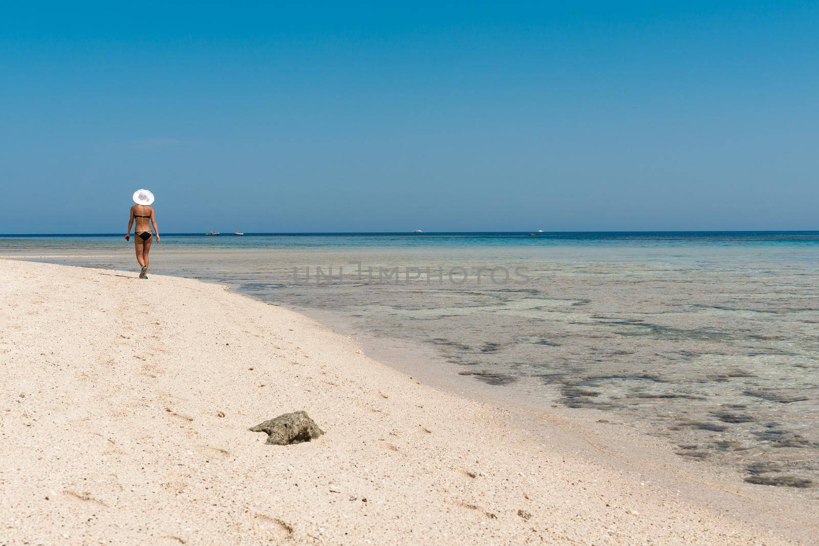 Slim woman wearing white hat walking along beautiful beach