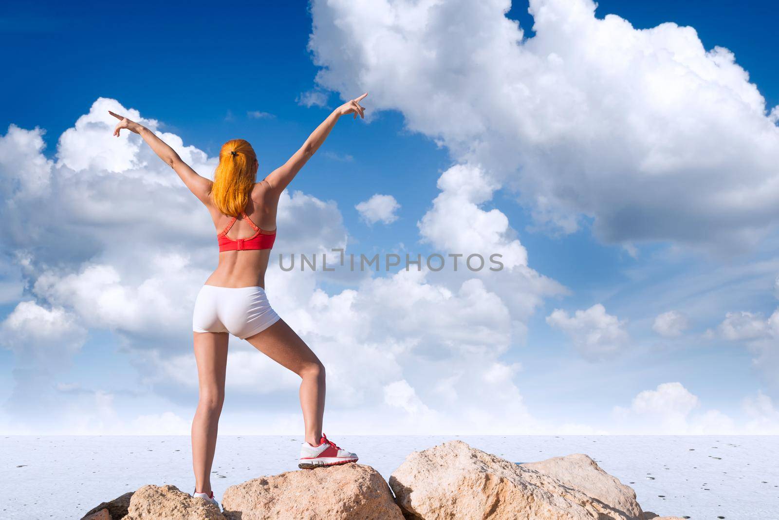 Fit young woman with raised hands above the desert on top of mountain