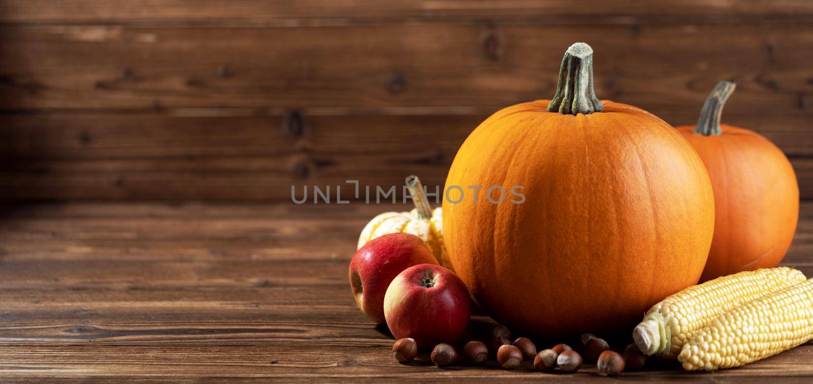 Autumn harvest still life with pumpkins, apples, hazelnut, corn on wooden background with copy space for text