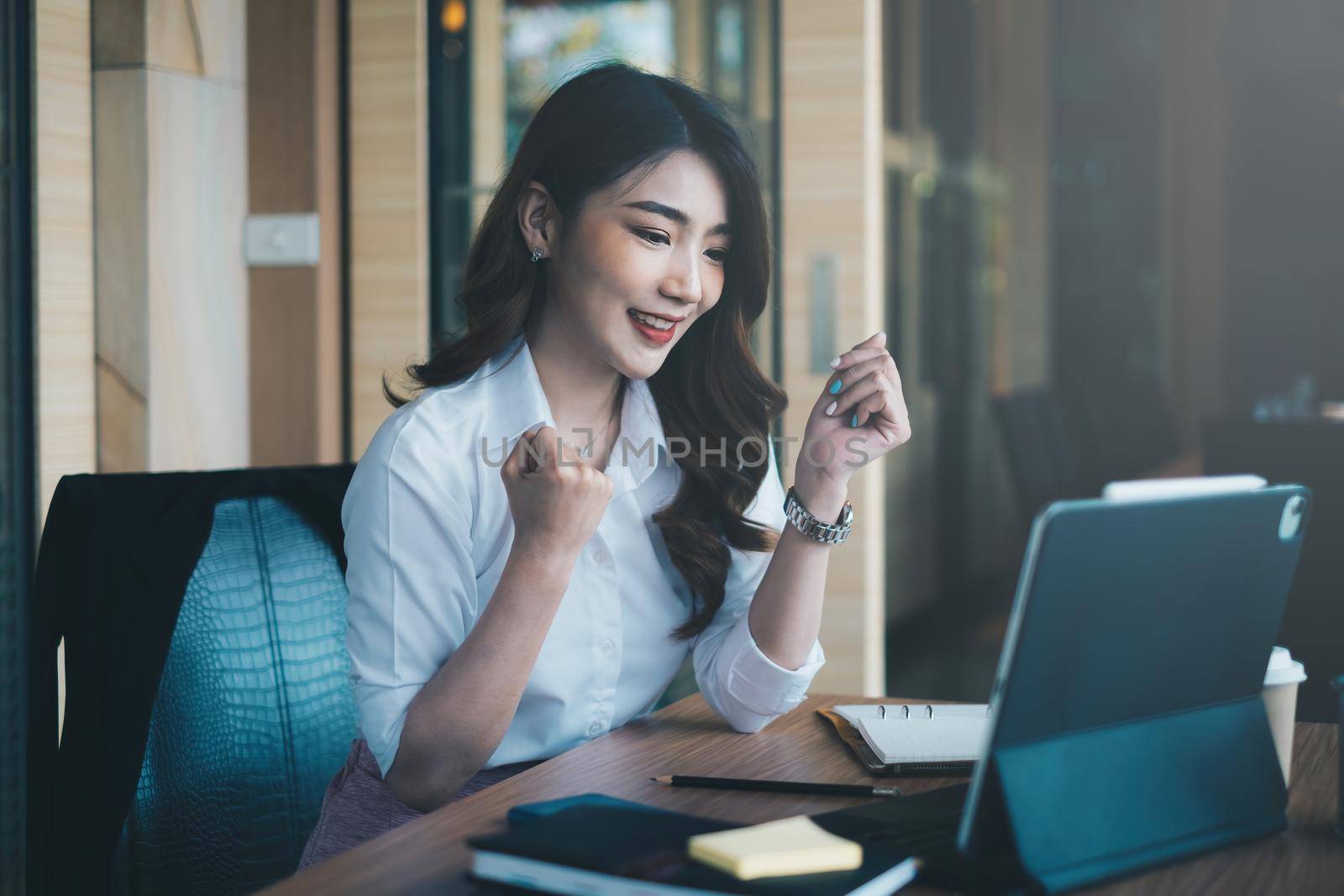 Excited asian woman sits at her workstation, ecstatic to have received a job offer following an interview by email on her laptop.