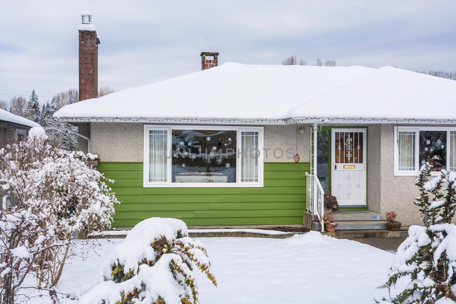 Family house with front yard in snow. Colorful residential house on winter cloudy day