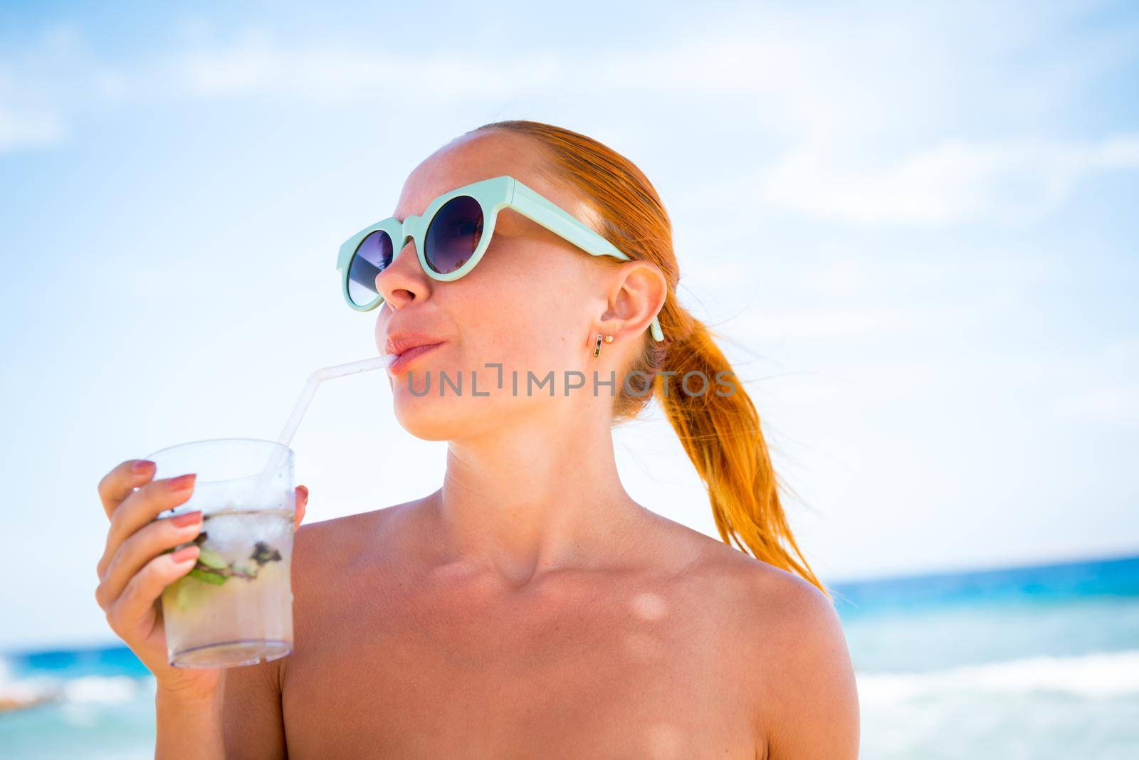 Young woman with glass of mojito wearing bikini at the beach