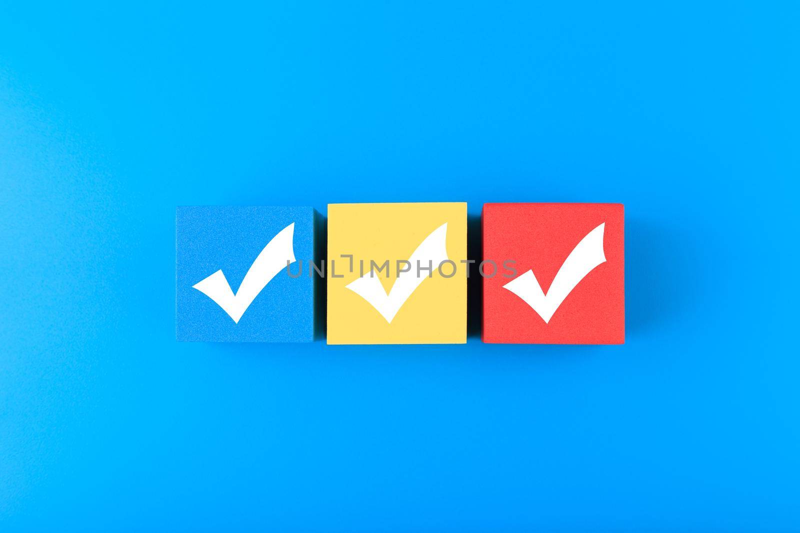 Three checkmarks on multicolored cubes in a row on blue background with copy space. Concept of questionary, checklist, to do list, planning, business or verification. Modern minimal composition