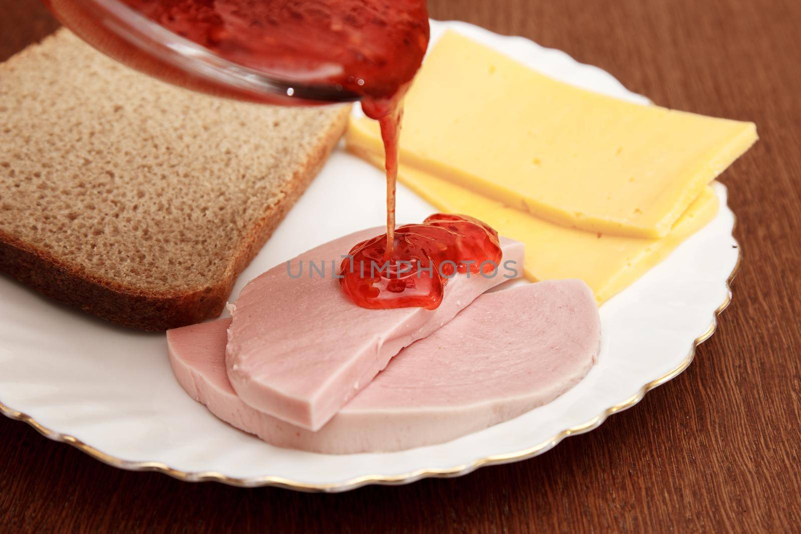 slices of cheese bread and sausage on a plate and saucer with hot chili sauce on wooden table. indoor closeup