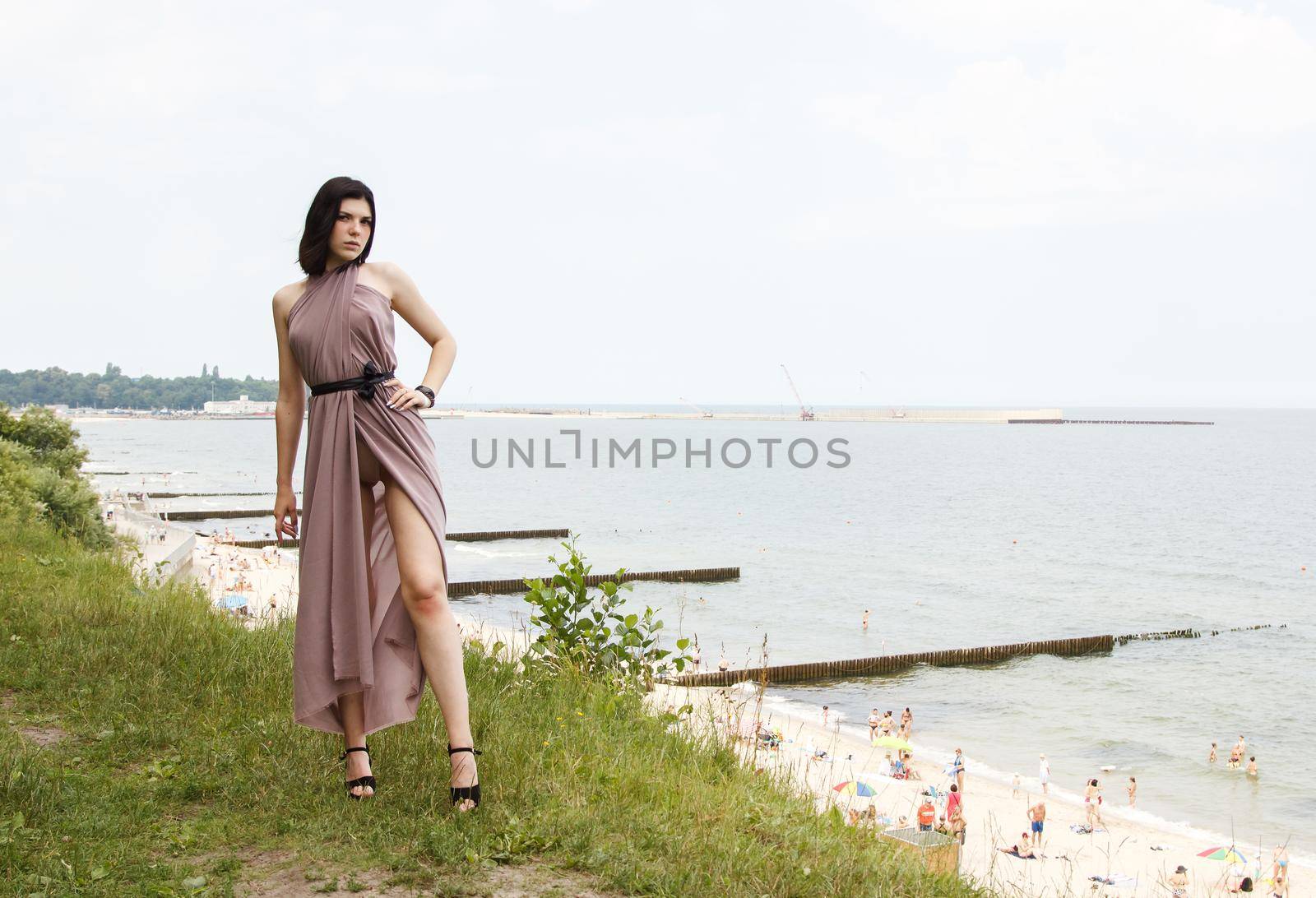 young brunette woman in beige dress standing by the sea on summer day