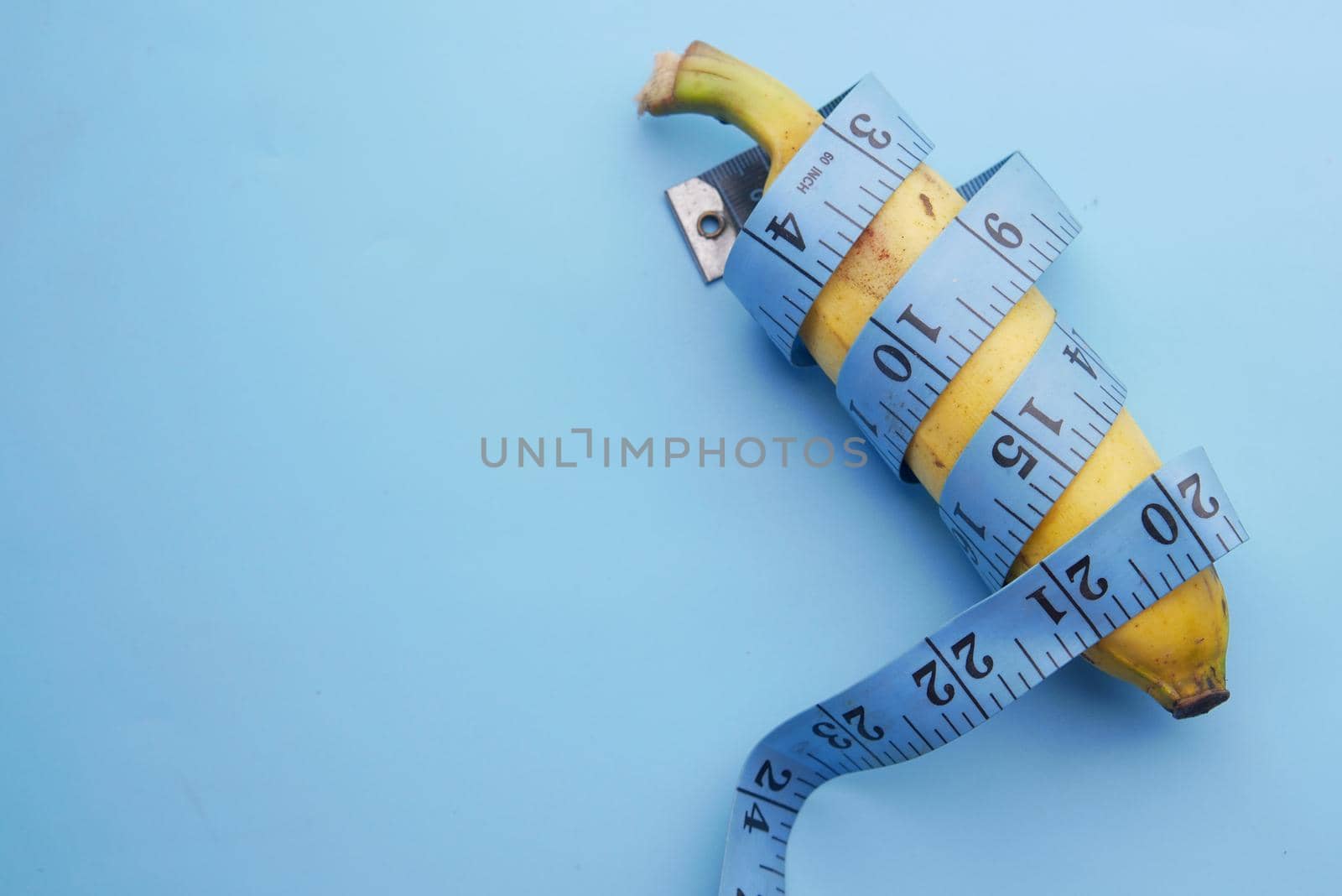 close up of measurement tape and banana on blue background .