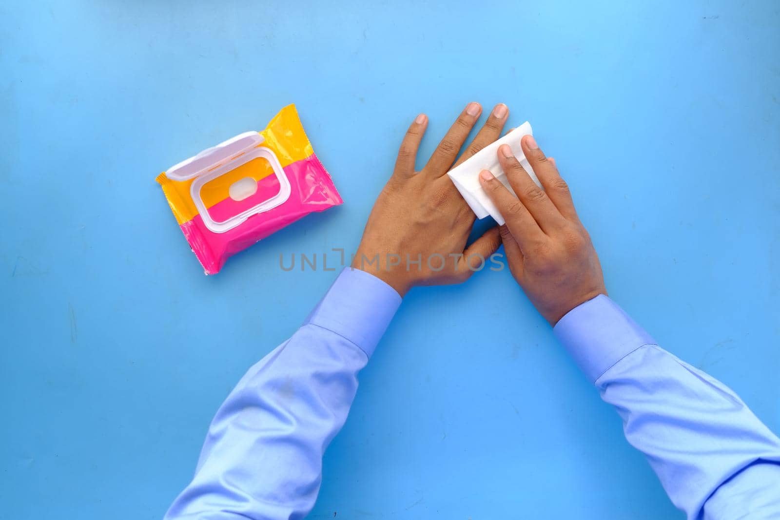 man disinfecting his hands with a wet wipe on blue background by towfiq007