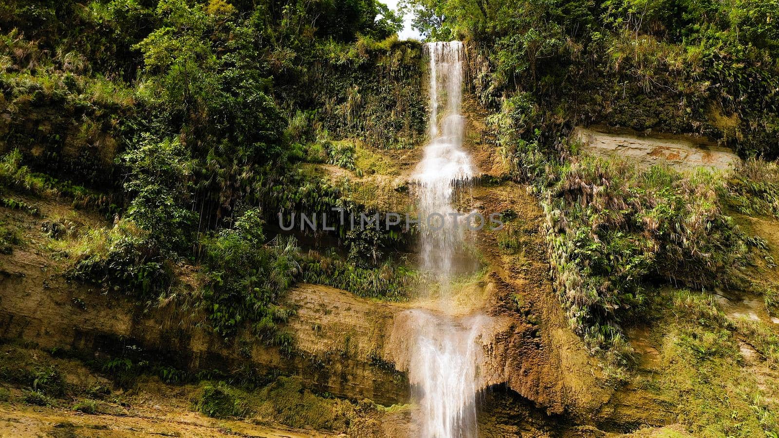 Aerial top view of jungle Waterfall in a tropical forest surrounded by green vegetation. Can-umantad Falls in mountain jungle. Bohol, Philippines.