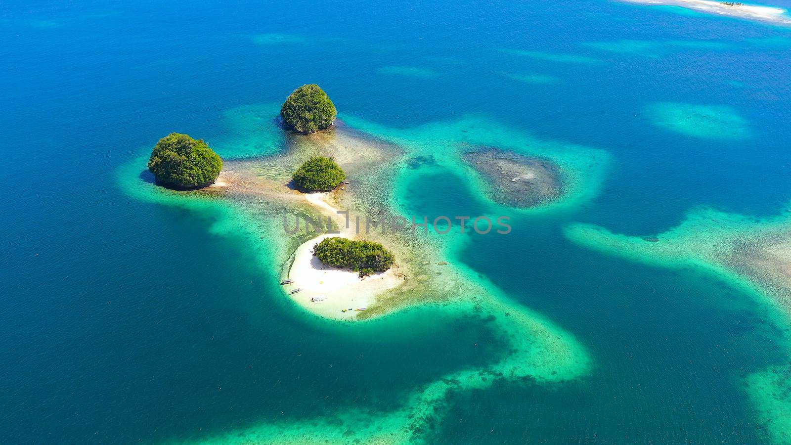 Small Island with beautiful beach, palm trees by turquoise water view from above. Britania Islands, Surigao del Sur, Philippines.