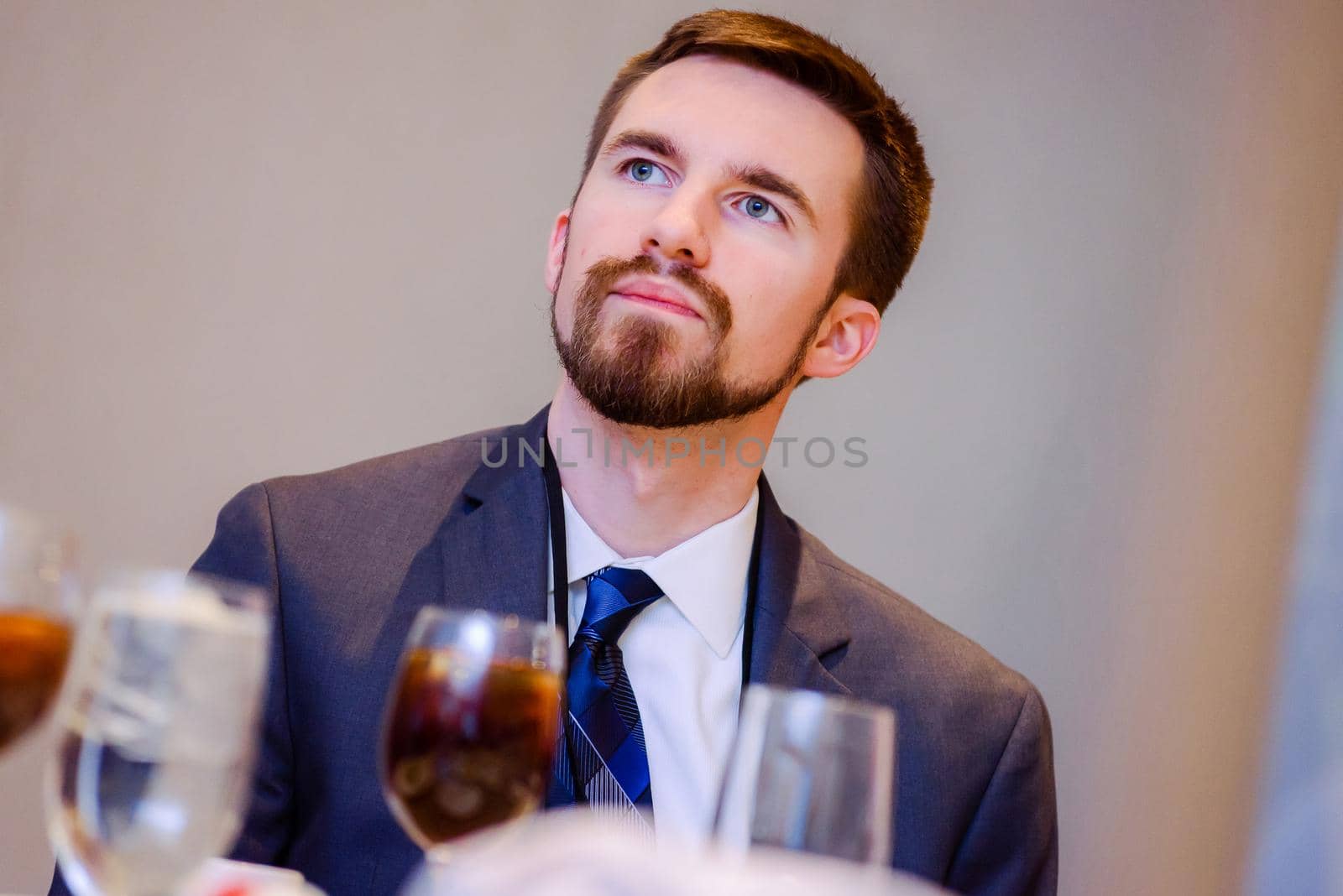Handsome man with dark hair and goatee looking up at speaker at a conference while sitting at dining table
