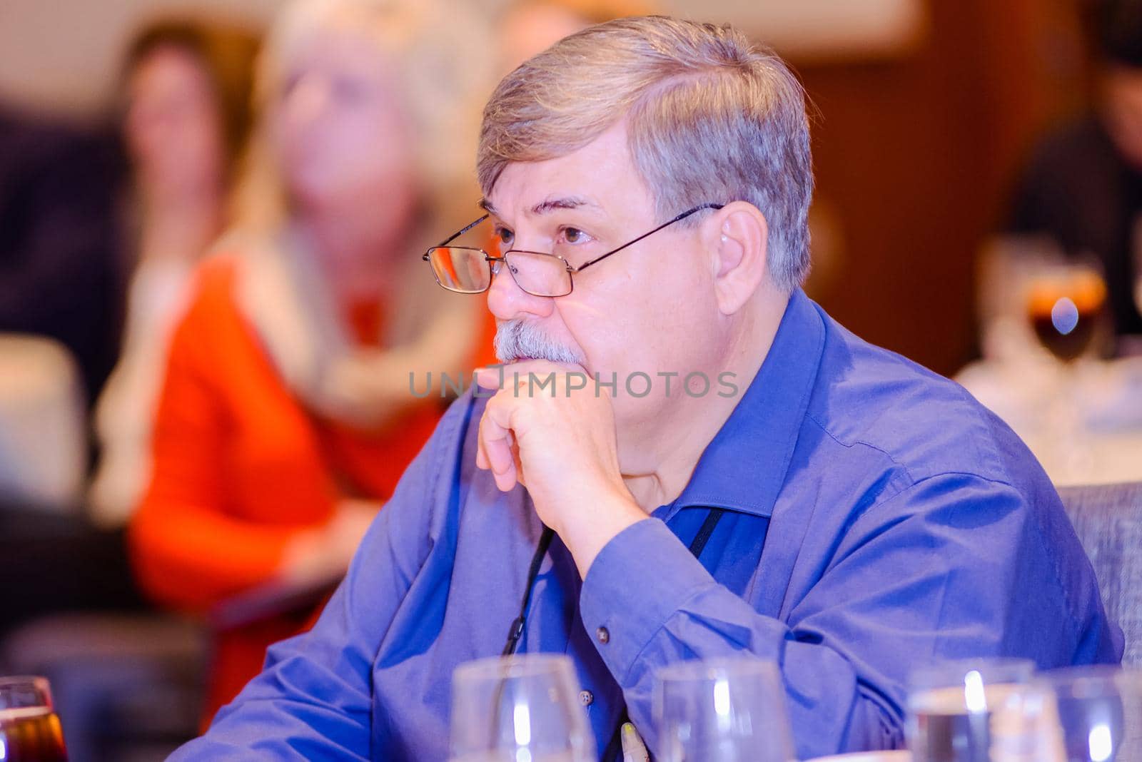 Older gentleman with mustache resting face on hand while being attentive at a conference.