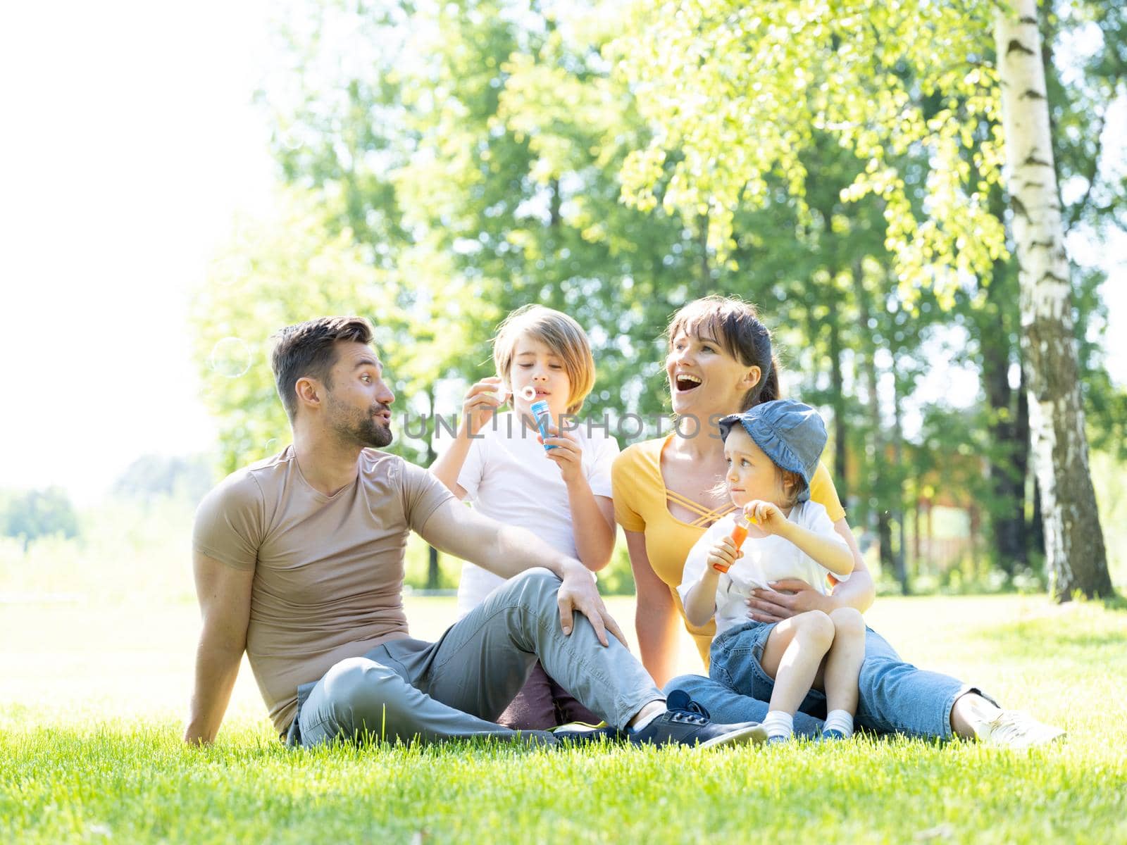 Happy family of mother, father and two children blowing bubbles in summer park