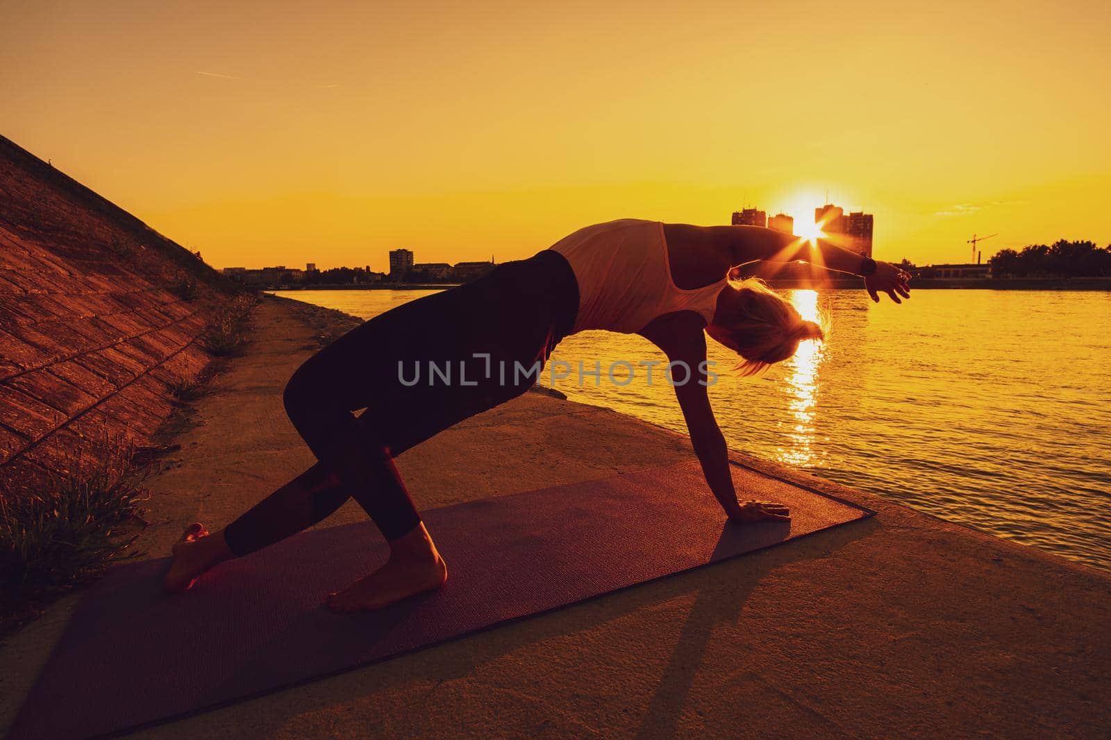 Young woman is exercising outdoor. She is practicing yoga on sunny day. Camatkarasana, Wild Thing yoga pose.