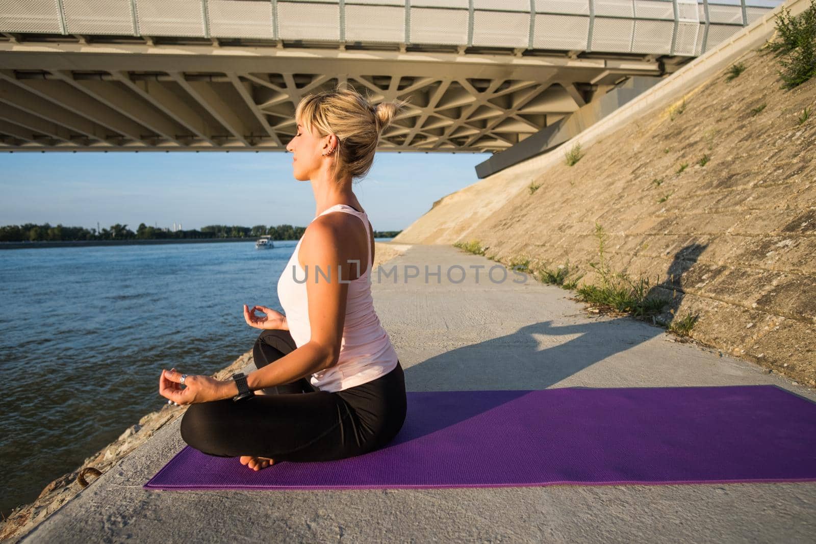 Young woman is exercising outdoor. She is practicing yoga on sunny day. Padmasana, Lotus pose.
