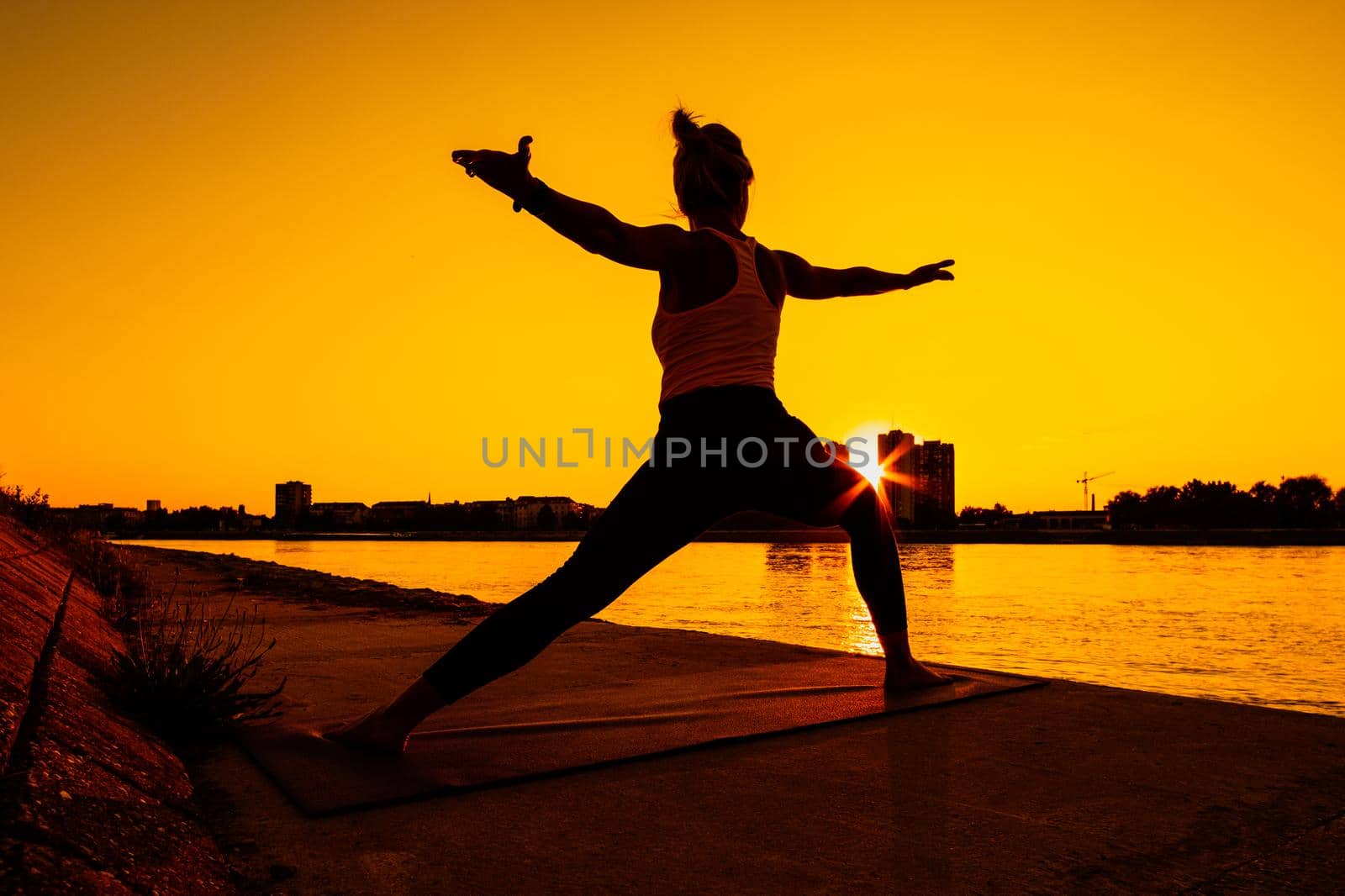 Young woman is exercising outdoor. She is practicing yoga on sunny day. Virabhadrasana / Warrior 2 pose.