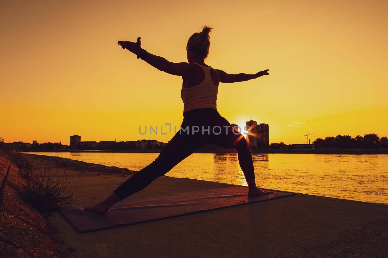 Young woman is exercising outdoor. She is practicing yoga on sunny day. Virabhadrasana / Warrior 2 pose.