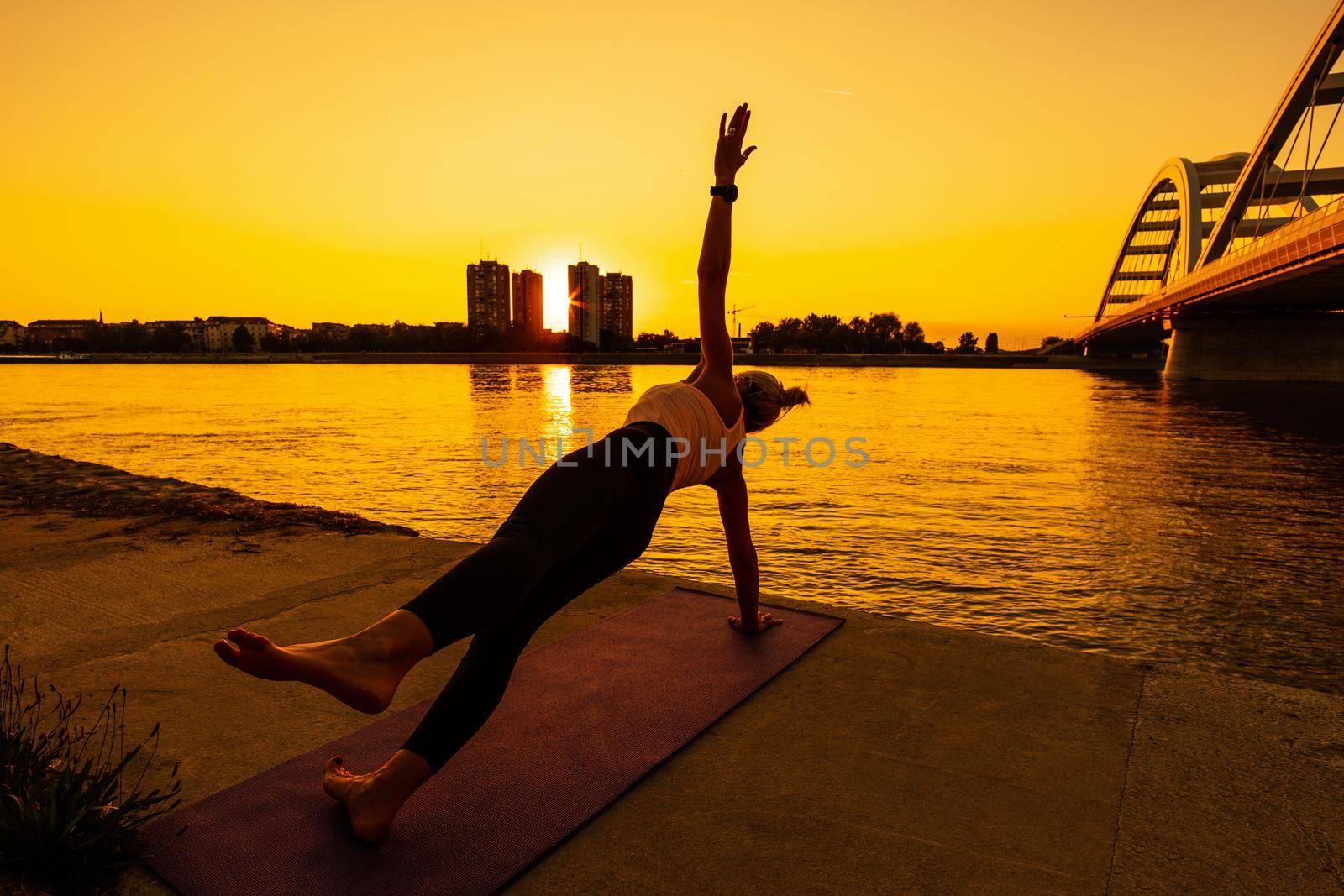 Woman exercising pilates on sunny day. Side plank with leg kick exercise.