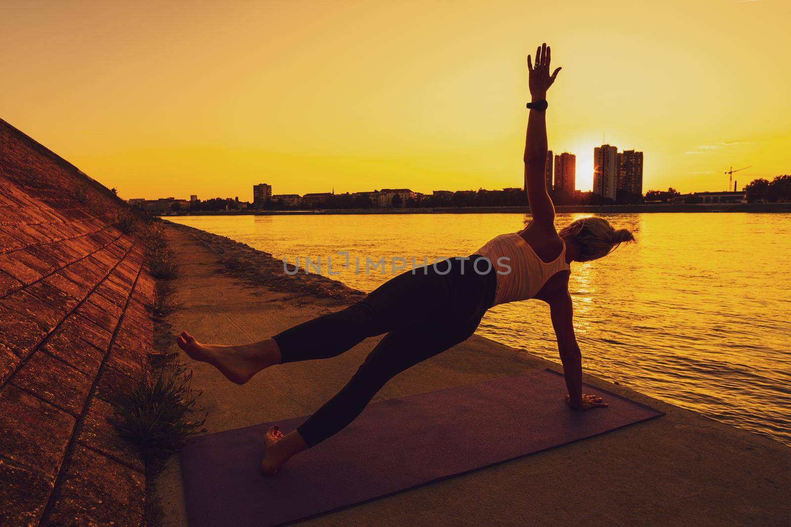 Woman exercising pilates on sunny day. Side plank with leg kick exercise.