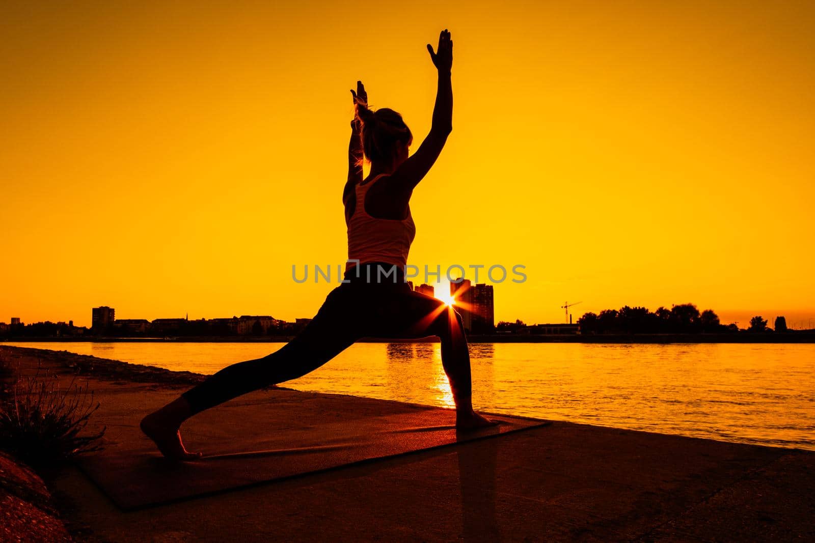 Young woman is exercising outdoor. She is practicing yoga on sunny day. Virabhadrasana / Variation of Warrior pose.