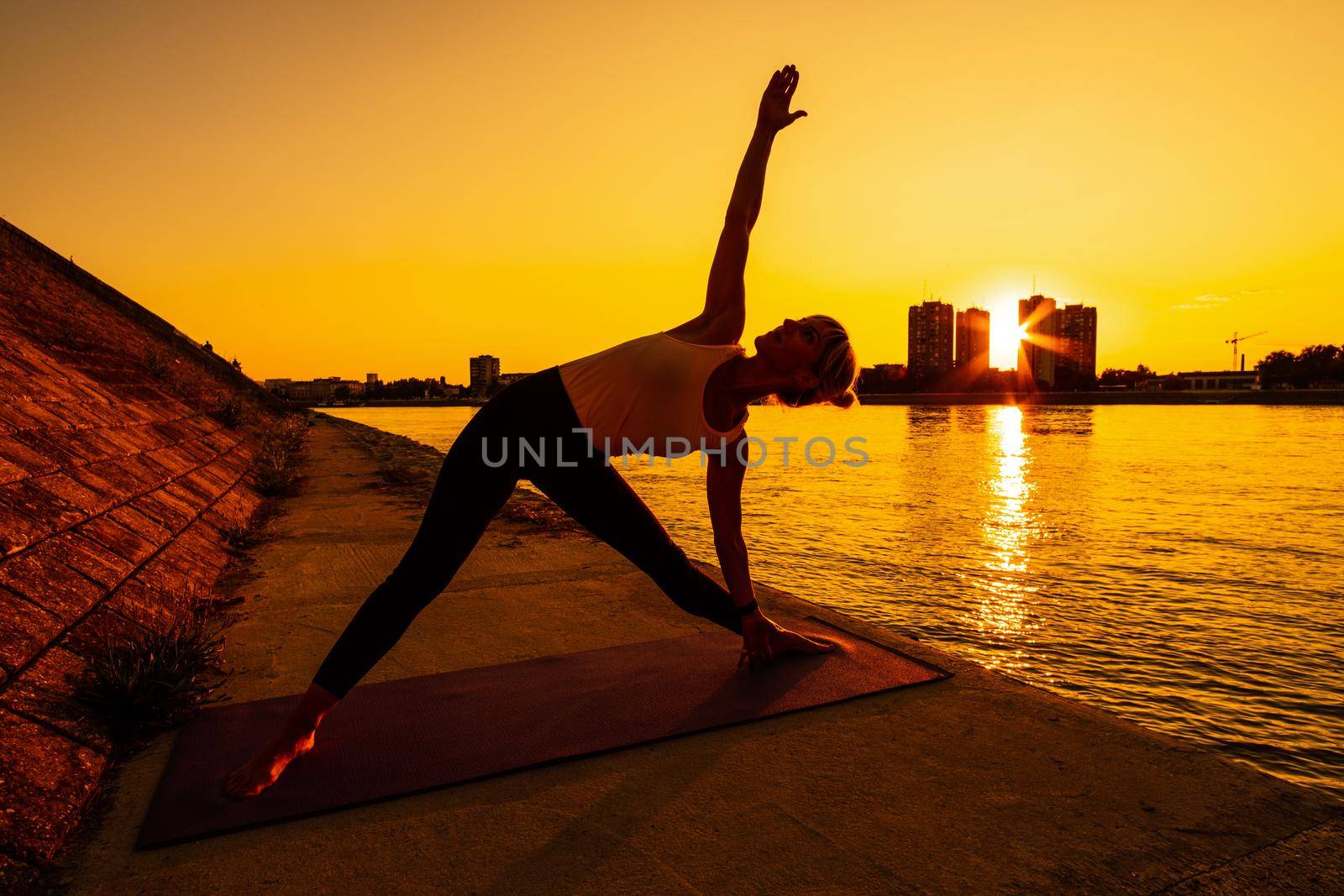 Young woman is exercising outdoor. She is practicing yoga on sunny day. Trikonasana, Bikram triangle left.