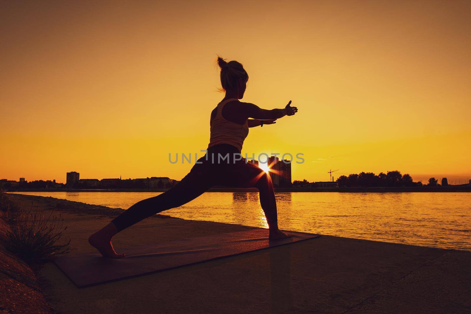 Young woman is exercising outdoor. She is practicing yoga on sunny day. Virabhadrasana / Variation of Warrior pose.