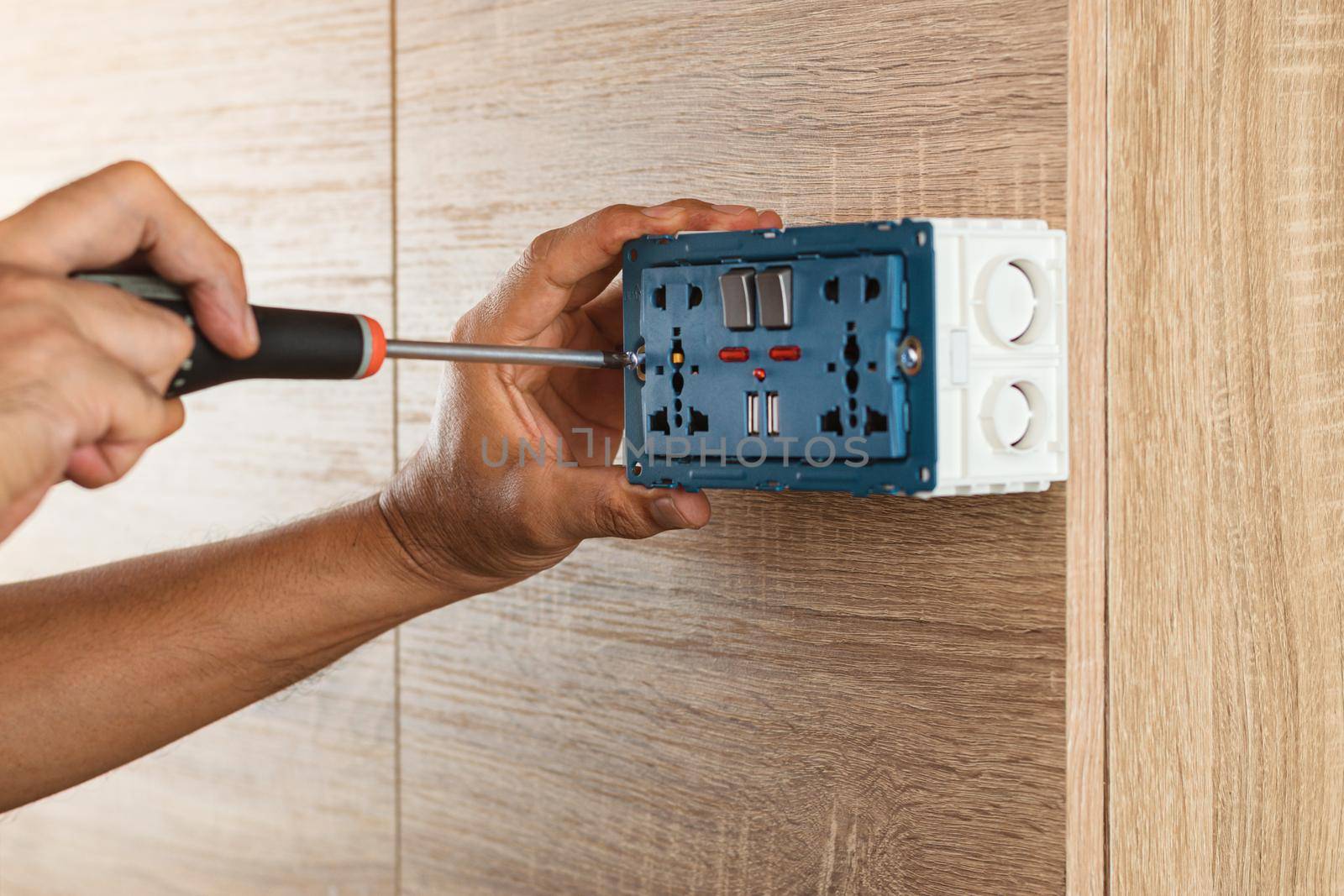 Electrician is using a screwdriver to install a power outlet in to a plastic box on a wooden wall. by wattanaphob