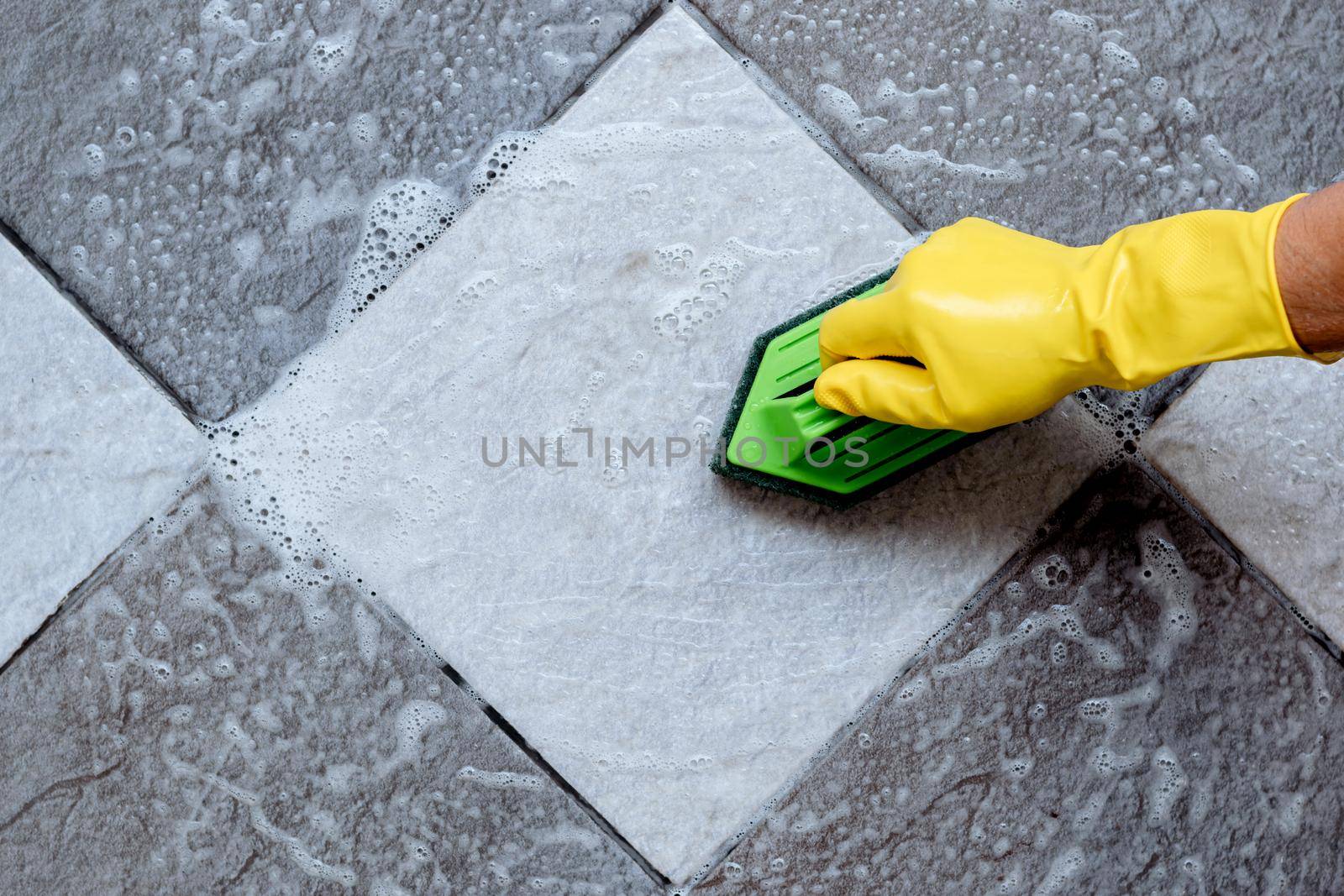 Cleaning the tiled floor with a green color plastic floor scrubber. by wattanaphob