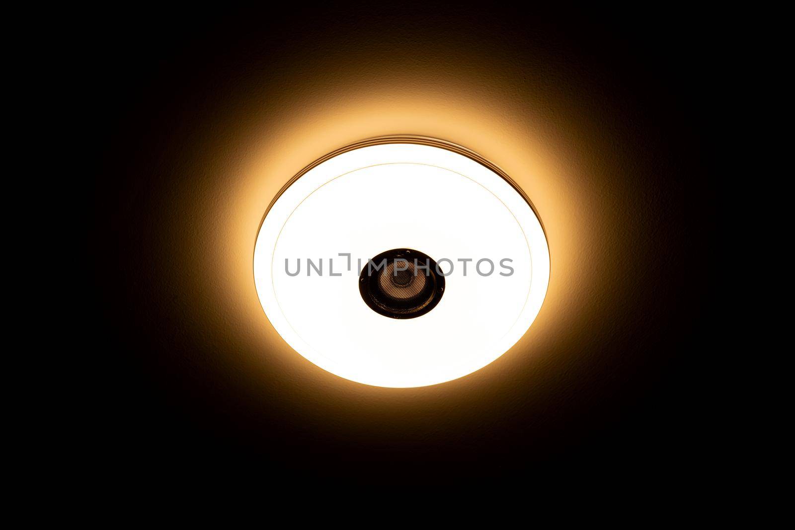 Warm light LED ceiling light with built-in wireless speakers over black background. by wattanaphob