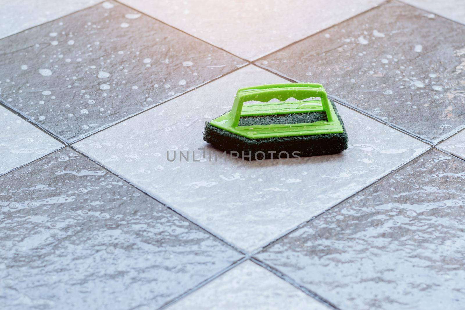 Close up a green plastic brush for scrubbing and cleaning floors placed on a wet tiled floor. by wattanaphob