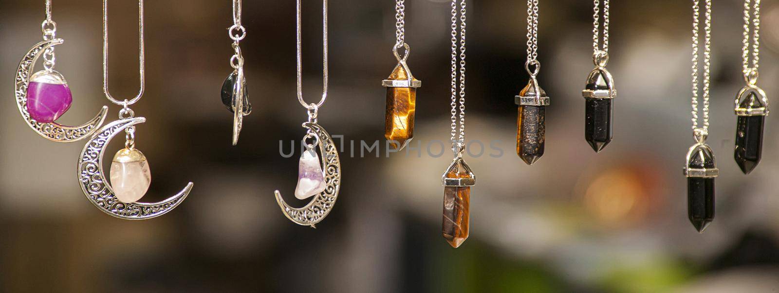 Miscellaneous silver necklaces of various shapes and colors set with colored stones on blurred background, banner image with copy space