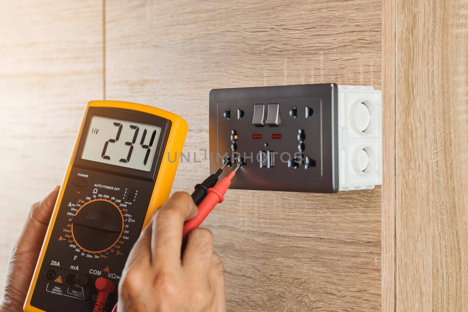 Electrician using a digital meter to measure the voltage at a wall socket on a wooden wall. by wattanaphob