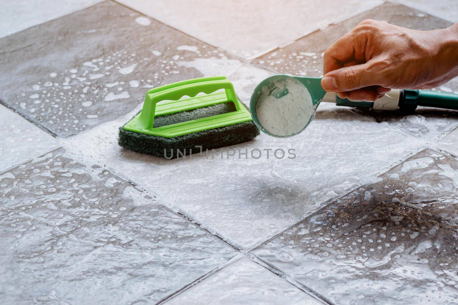 Close up a human hand pours detergent onto the wet tile floor to clean it. by wattanaphob